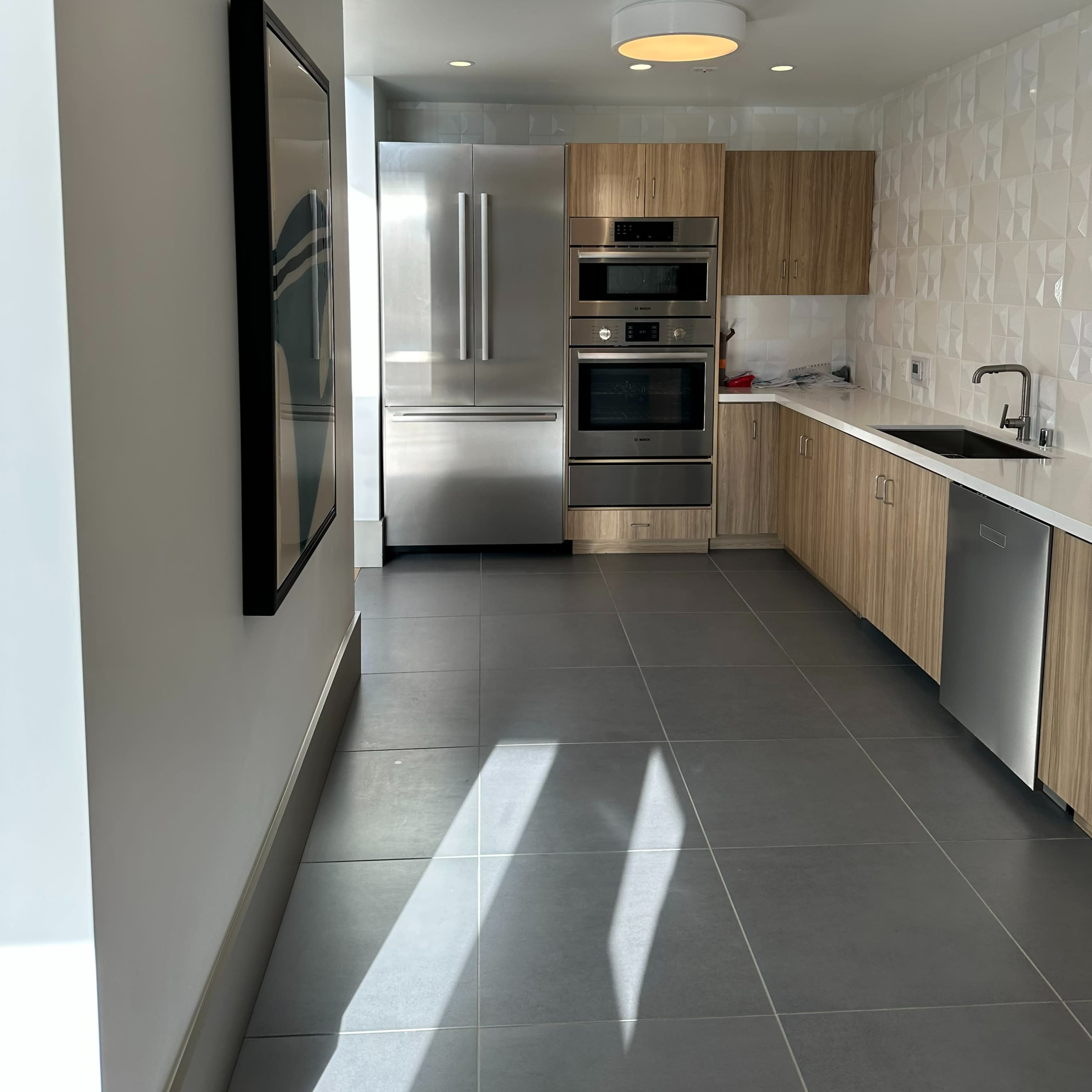 A modern kitchen with wooden cabinetry, stainless steel appliances, and gray tile flooring.