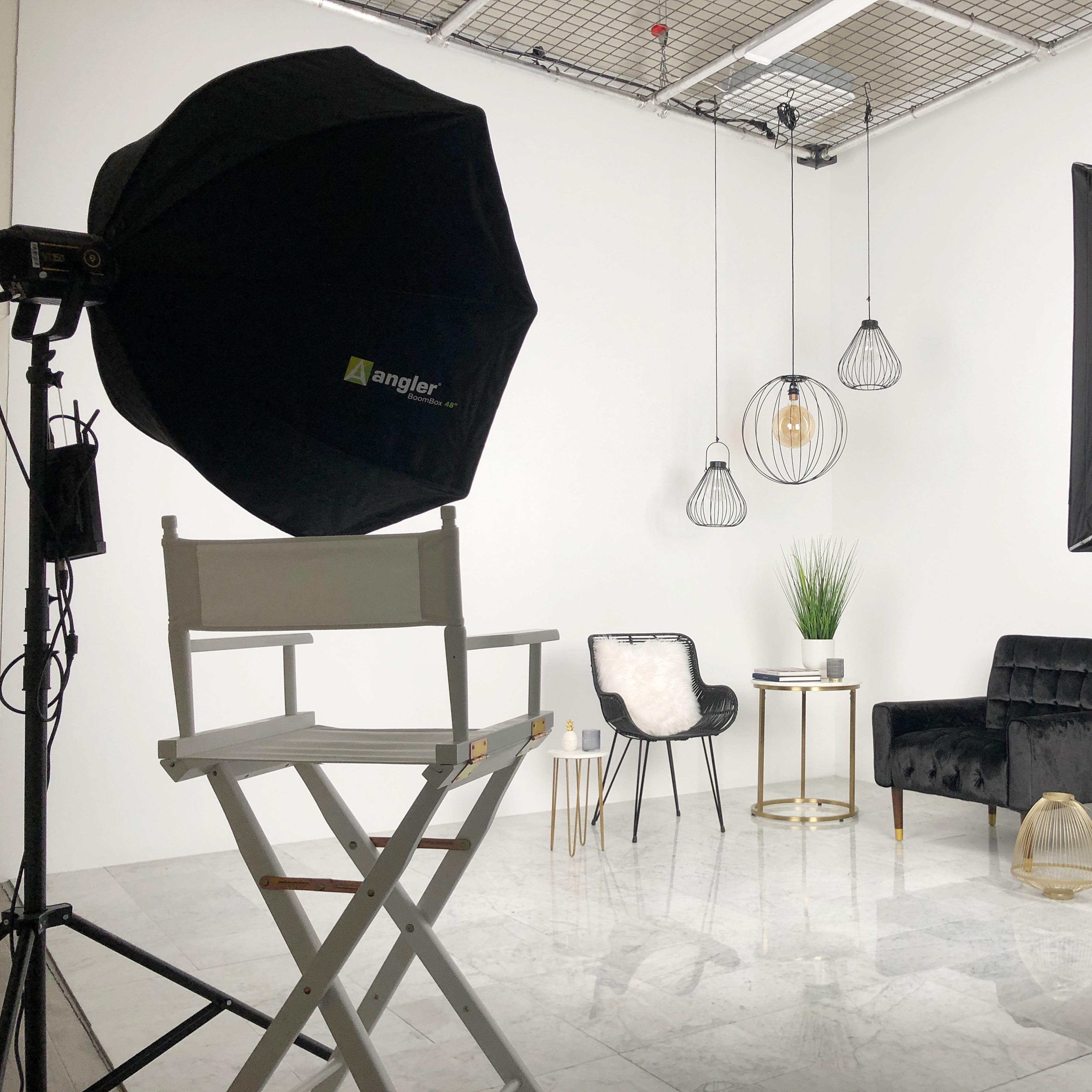 A photography studio setup with two light umbrellas, a director's chair, a small table, and a couch, all against a white backdrop.