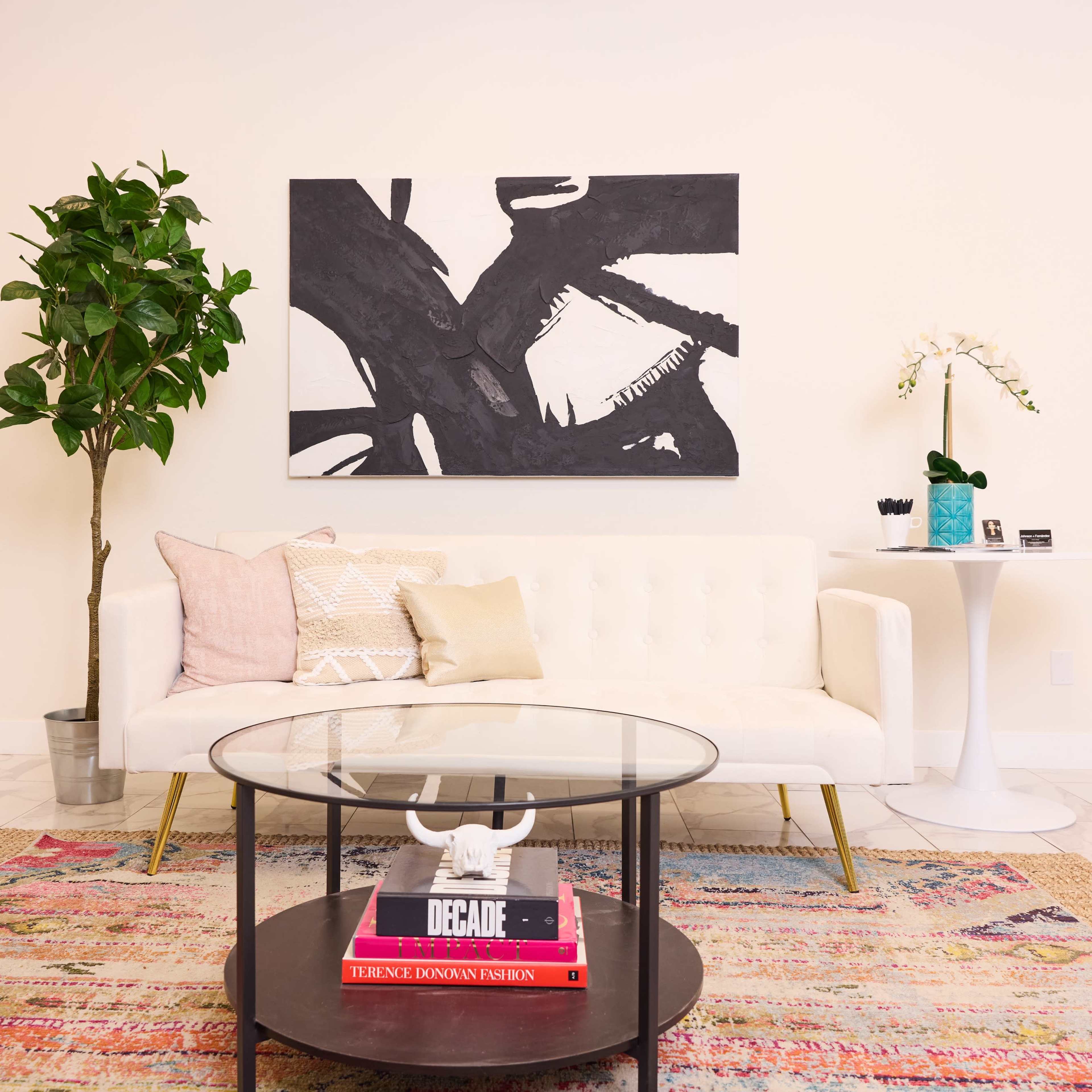 A modern living room with a white sofa, a circular glass coffee table, and a colorful patterned rug.