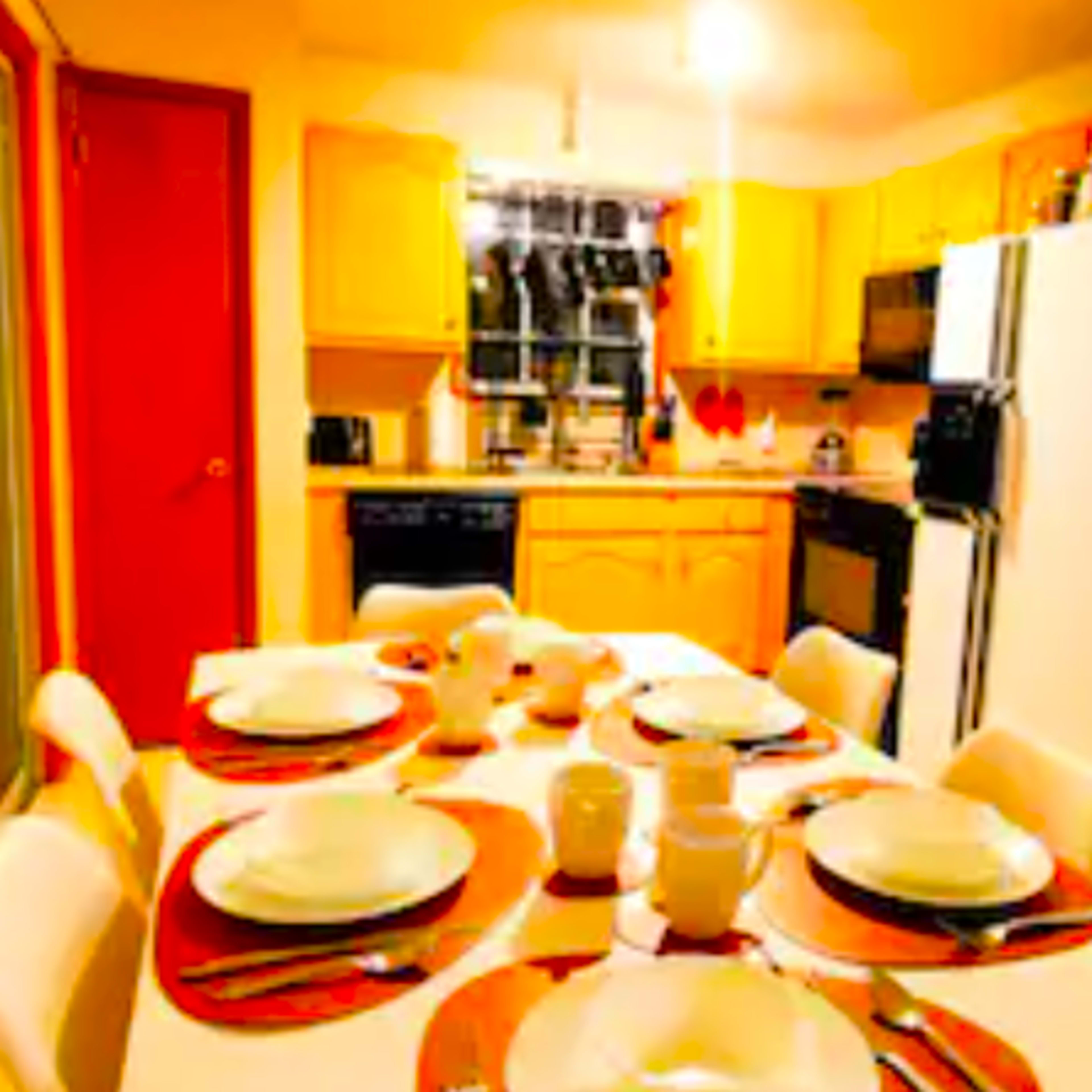 A dining table is set with plates and utensils in a kitchen featuring wooden cabinets and stainless steel appliances.