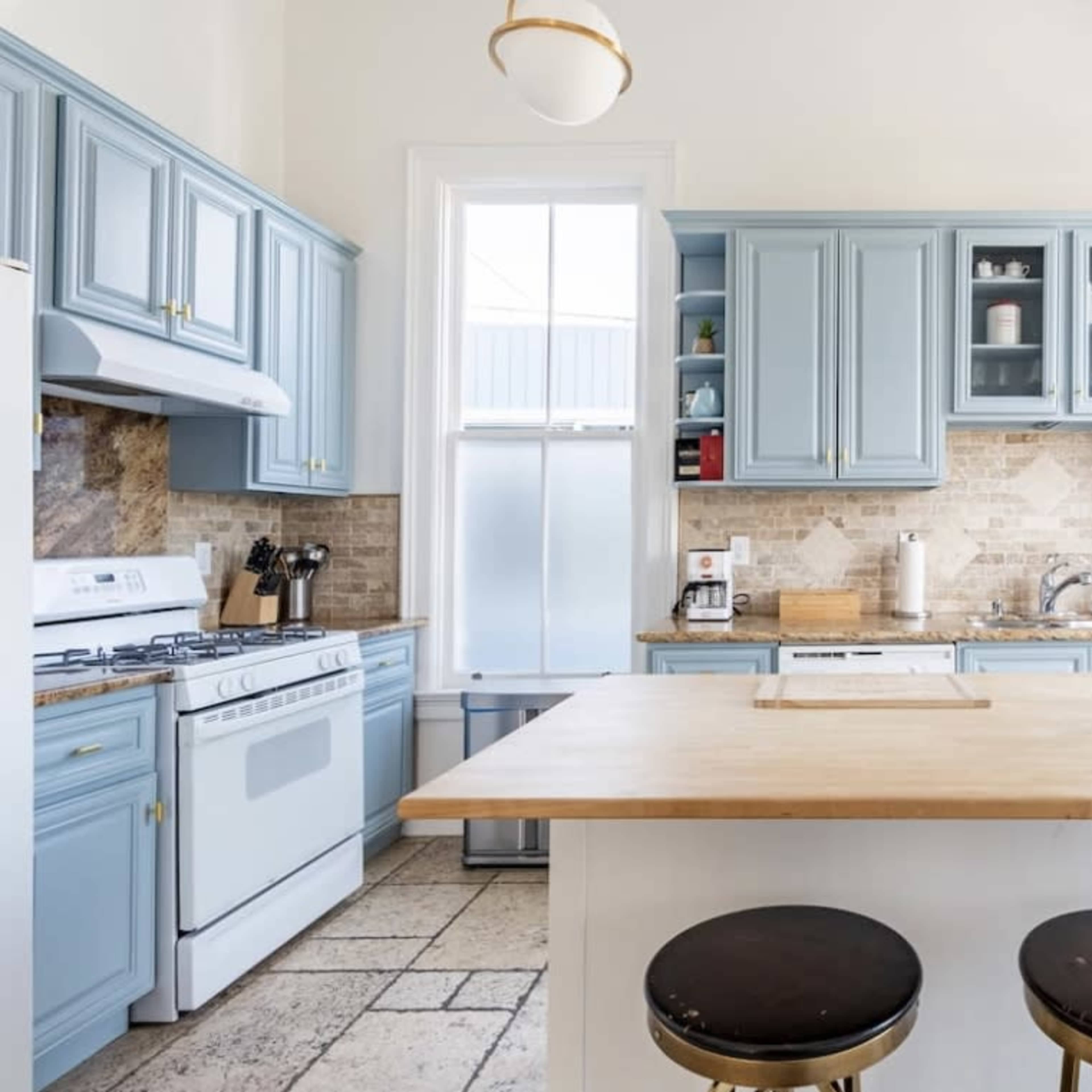 The kitchen features light blue cabinetry, a central wooden island, and a large window providing natural light.