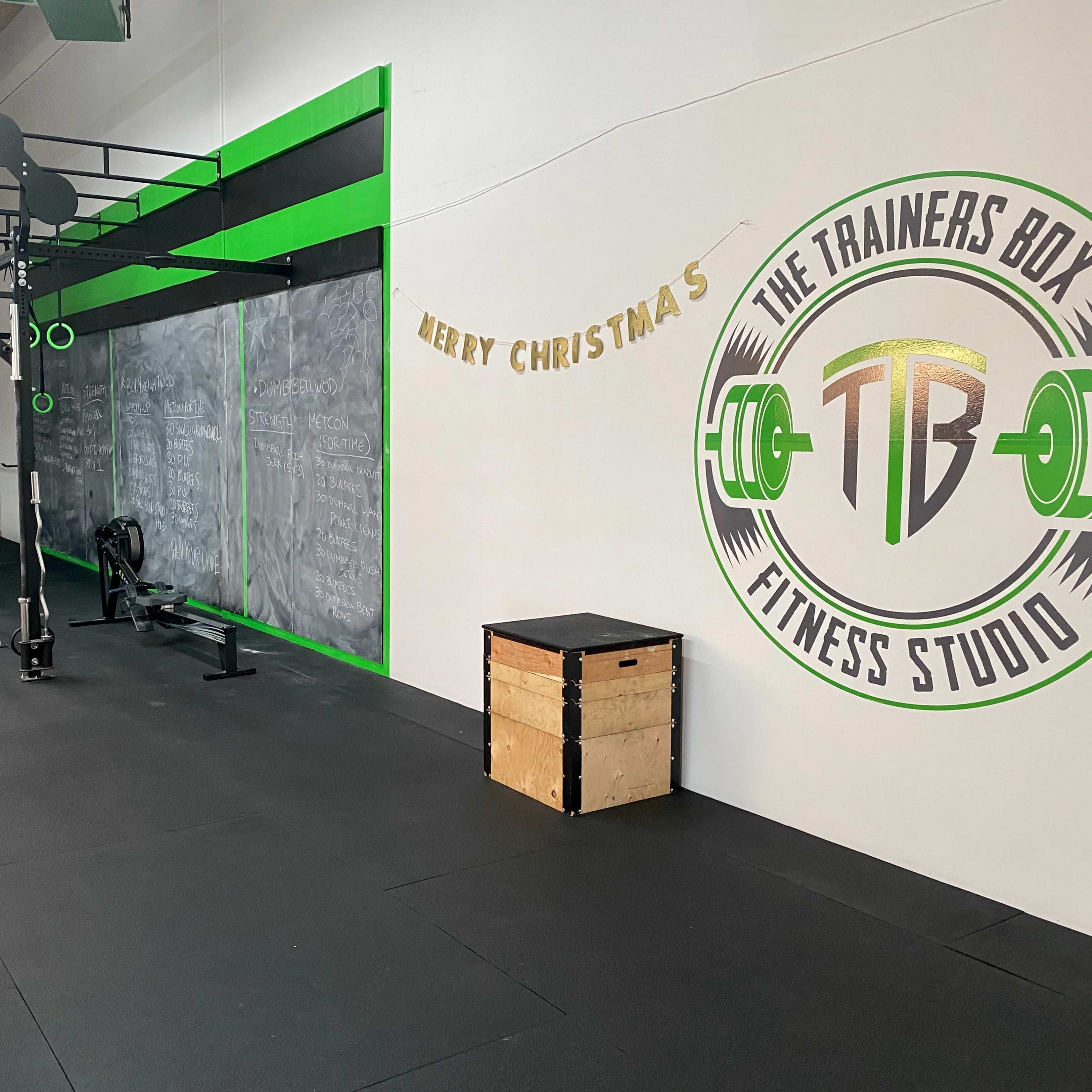 A fitness studio features a workout area with equipment like a rowing machine and dumbbells, alongside a decorated wall that says "Merry Christmas."