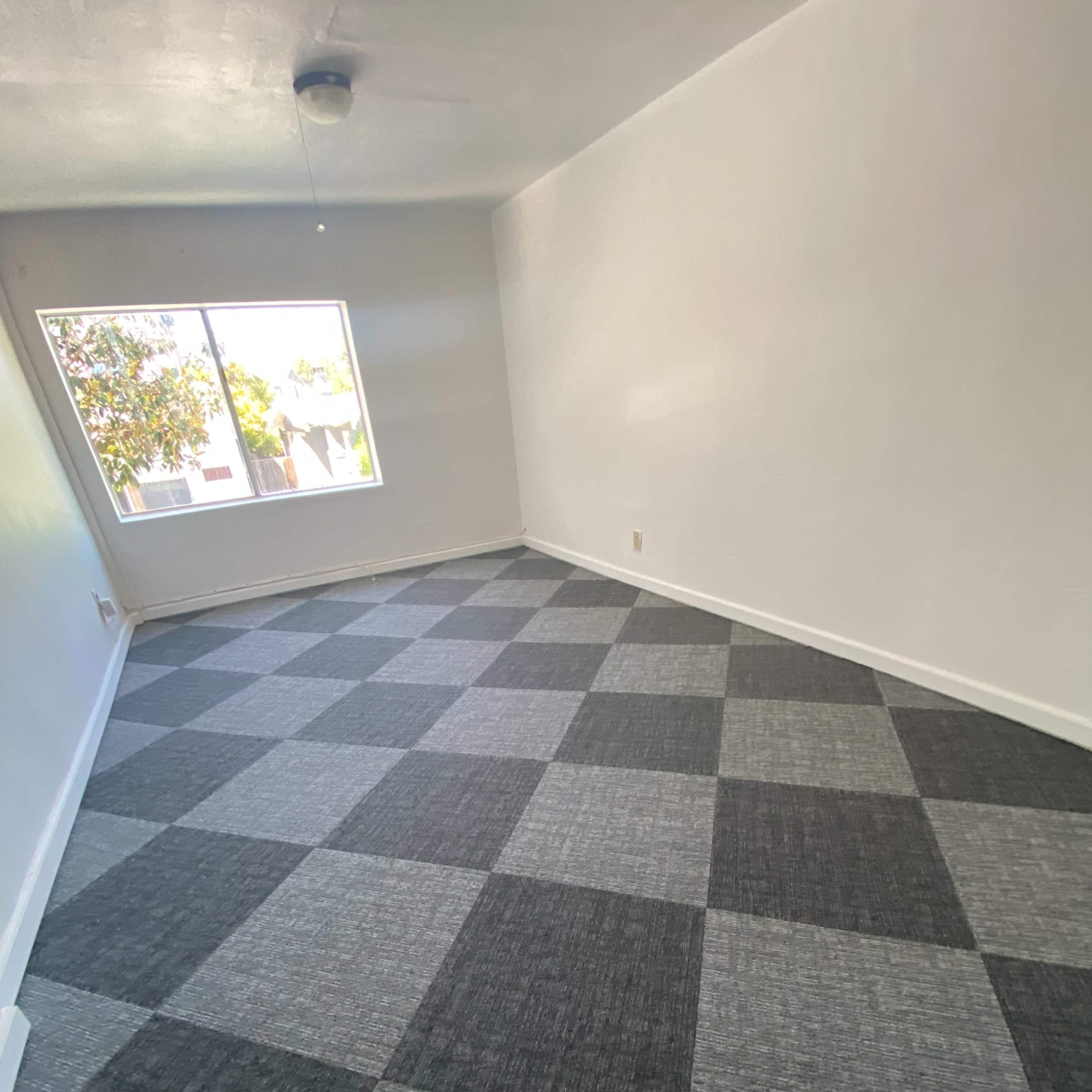 A room with a large window and checkered gray and black carpet flooring.