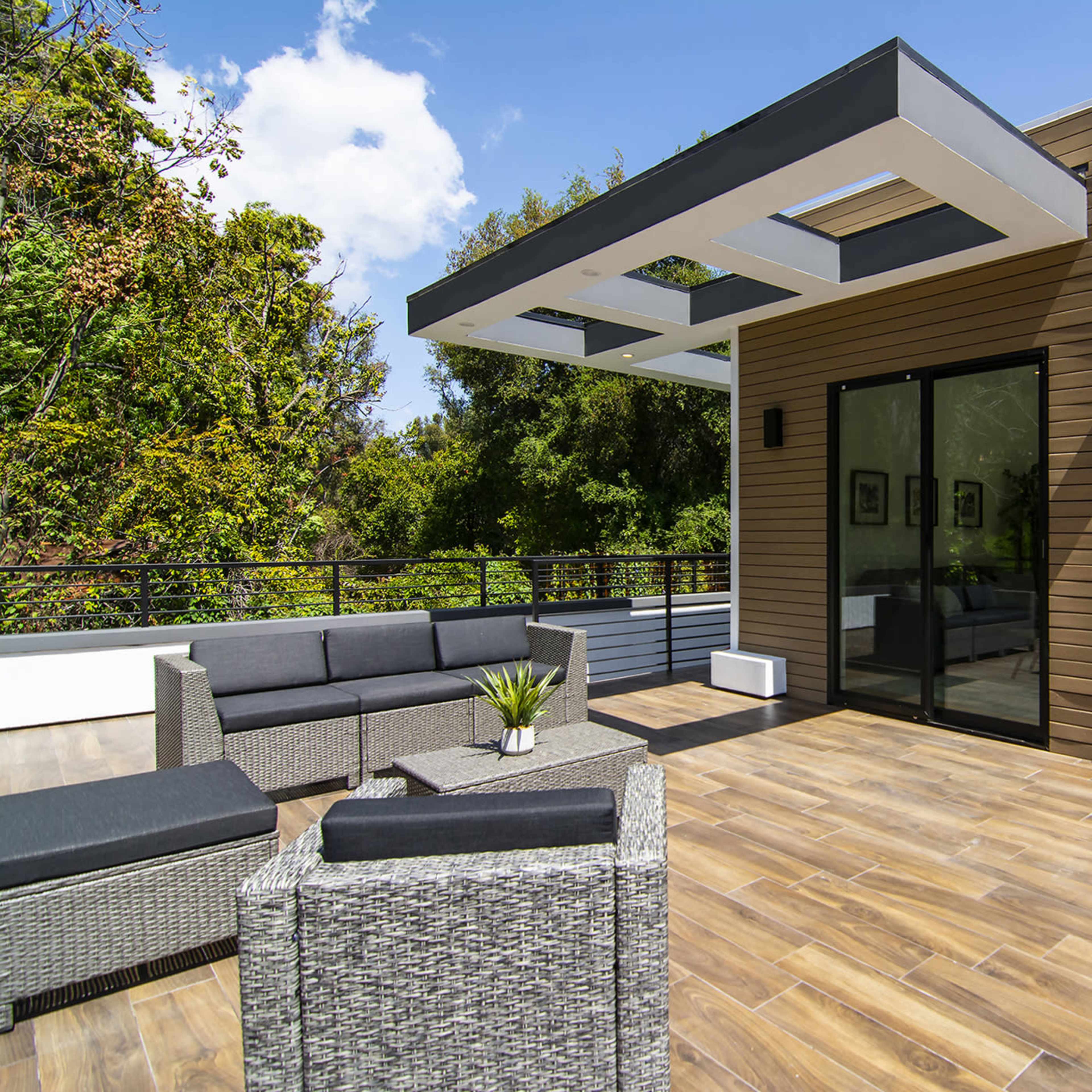A modern outdoor patio with a seating area, featuring a sleek canopy and wooden siding on the adjacent building.