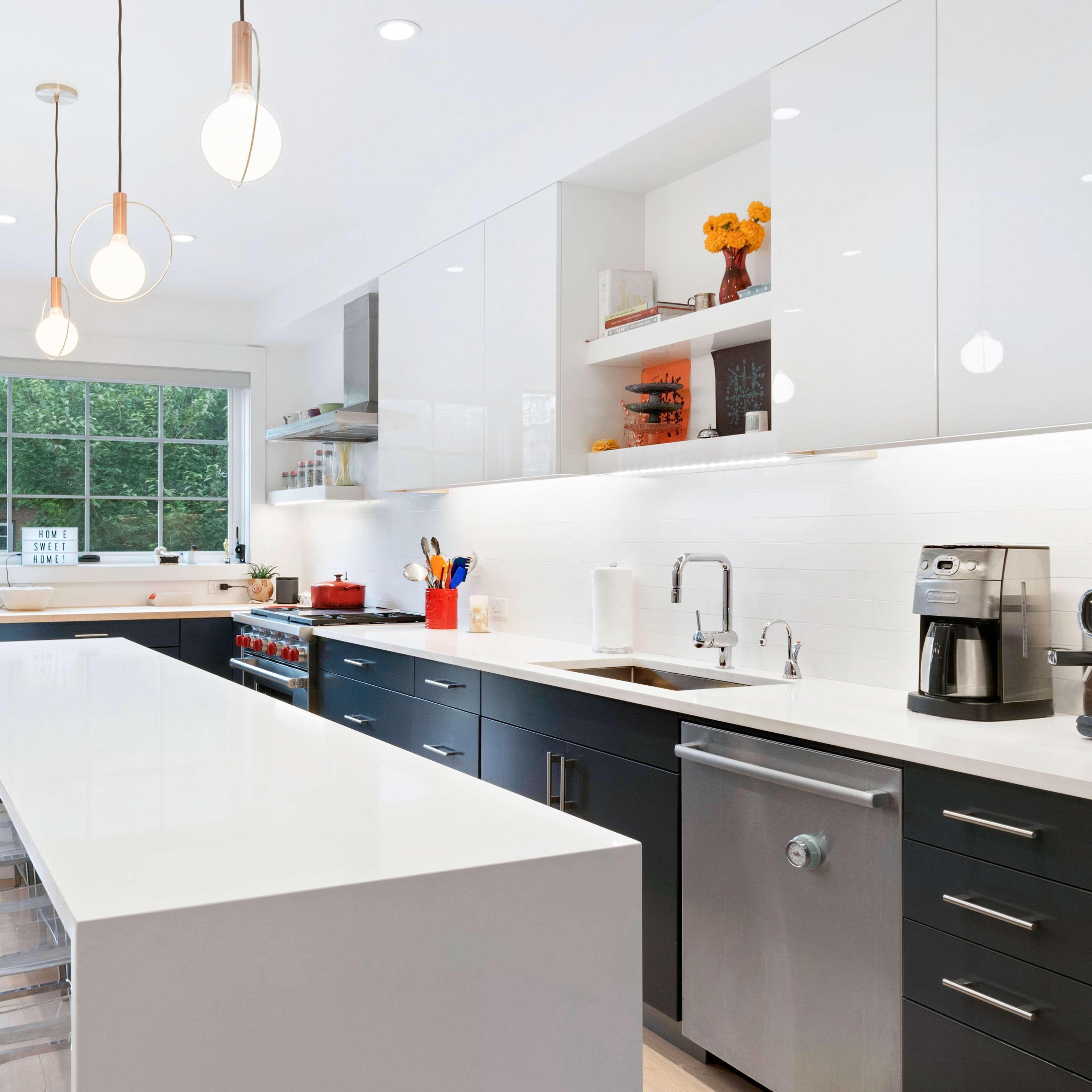 A modern kitchen features a large central island with seating, sleek cabinetry, and a window that opens to a green outdoor space.