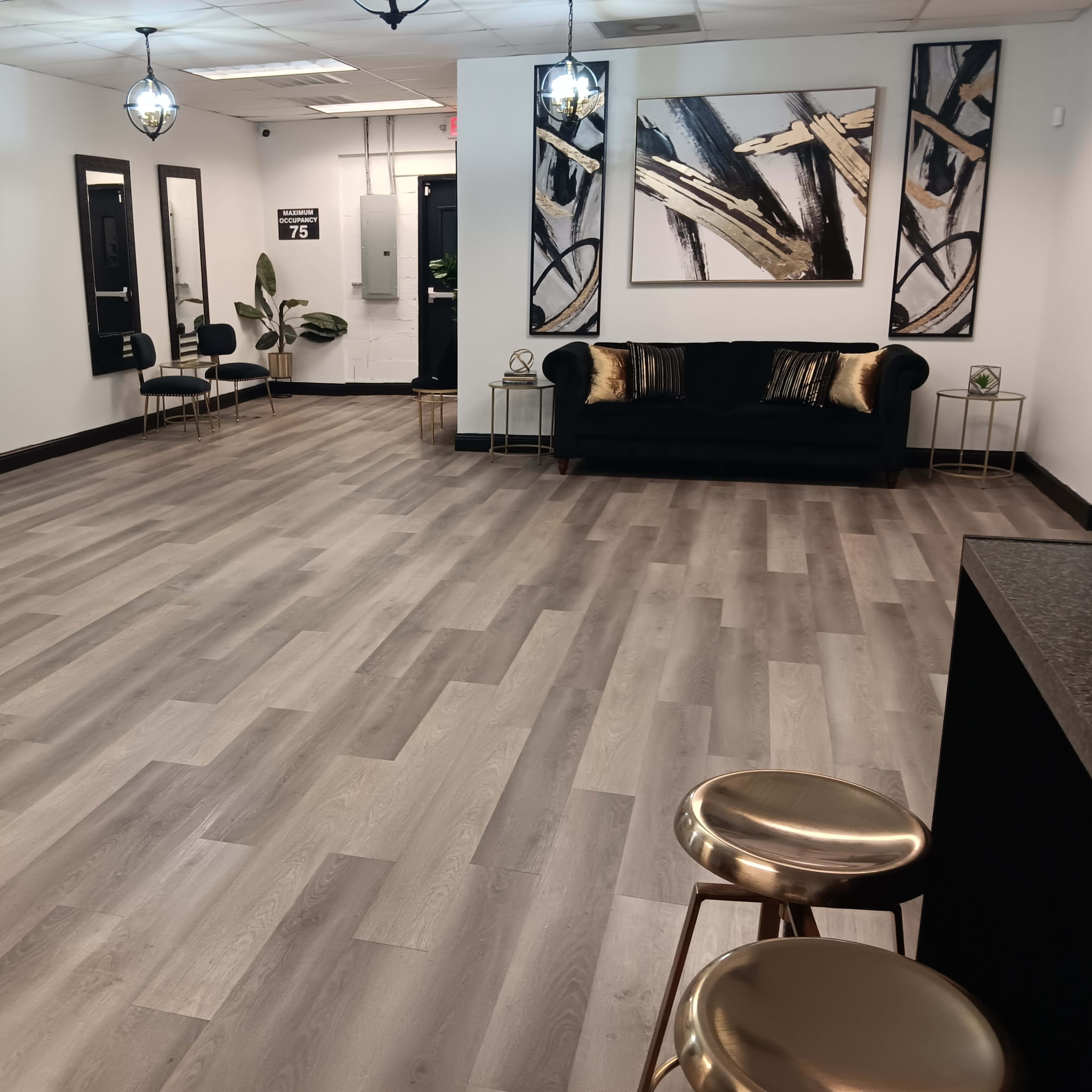 A spacious, modern interior with light wooden floors, black and gold furniture, and abstract wall art.
