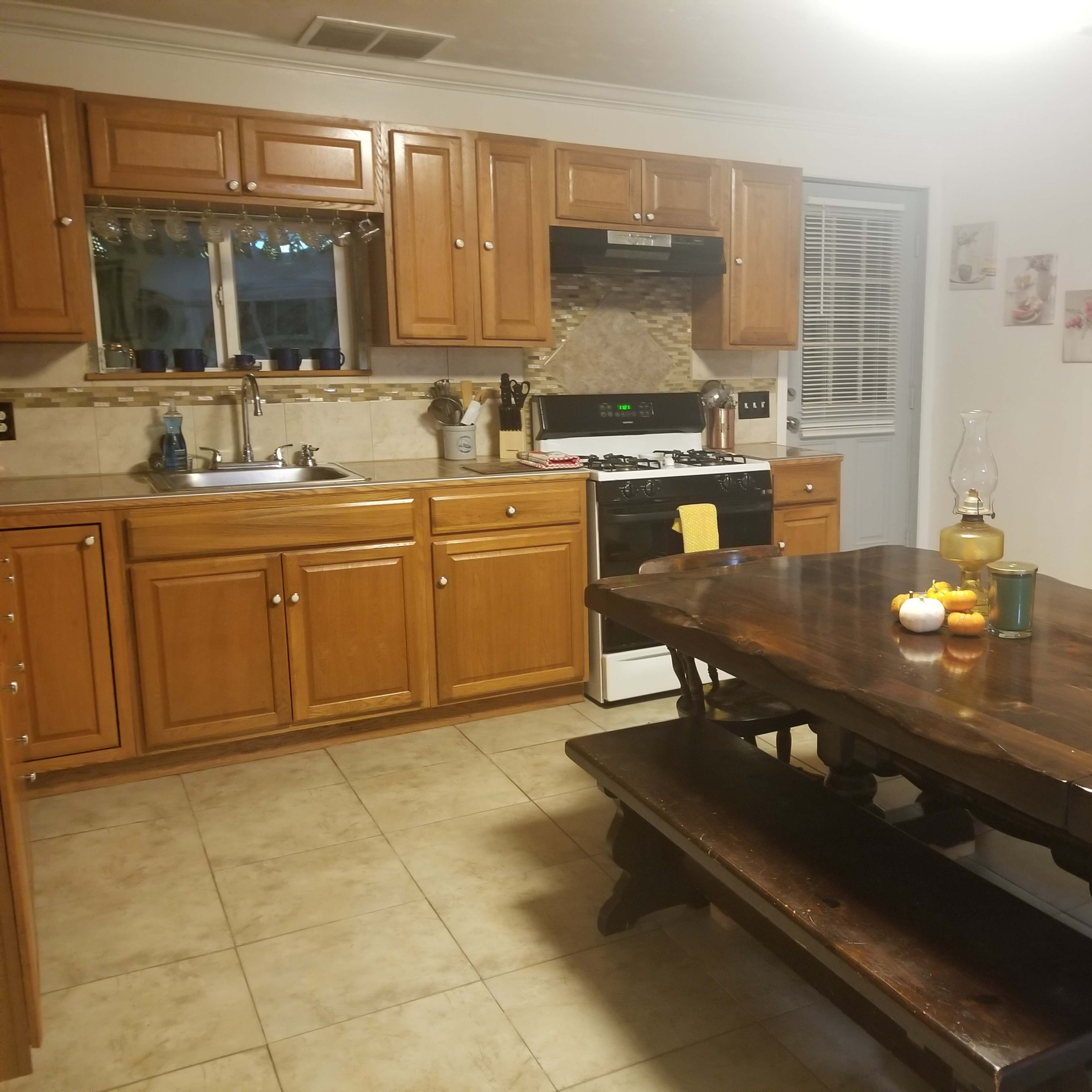 A kitchen with wooden cabinetry, a gas stove, and a large dining table set with candles and decorative items.