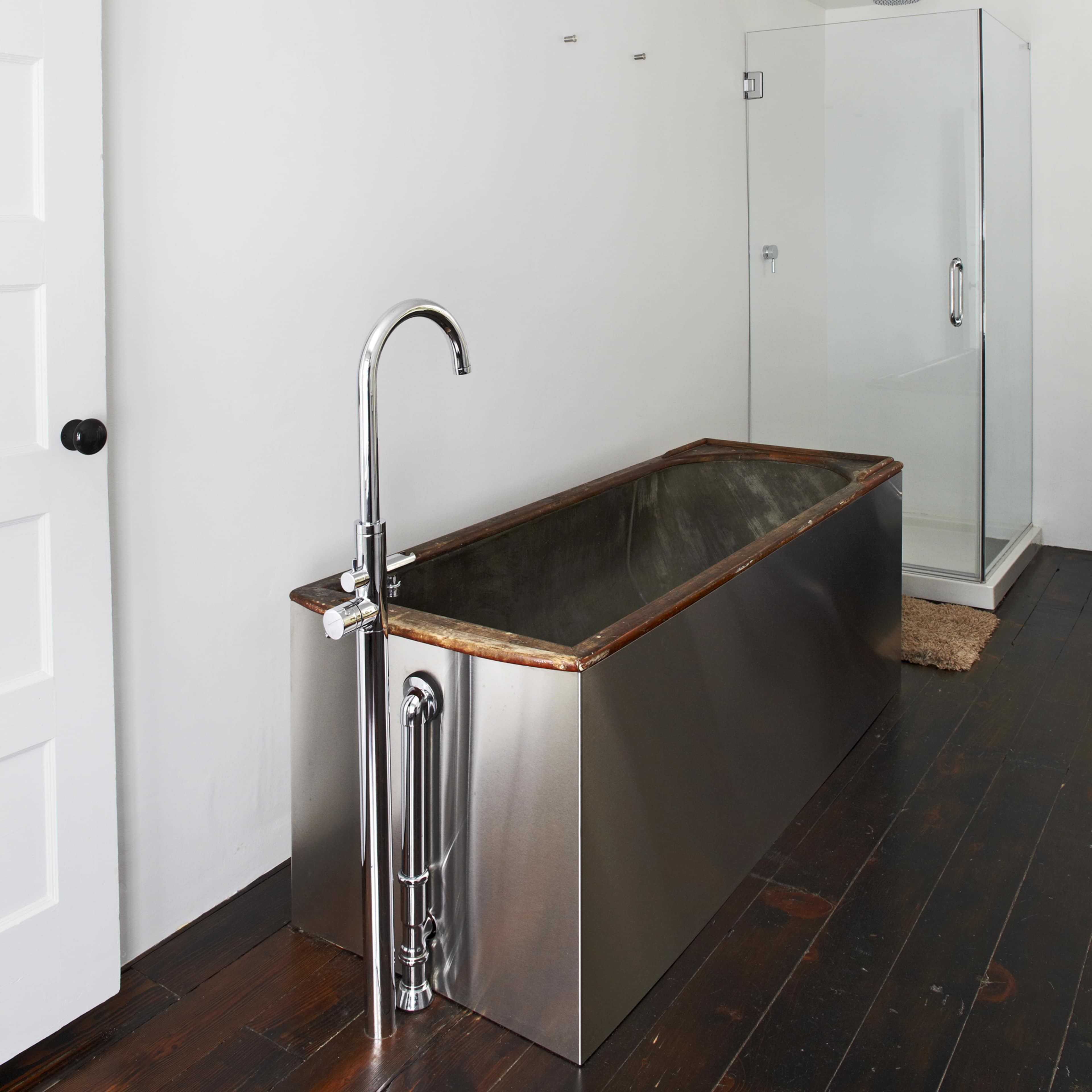 A modern bathroom with a stainless steel freestanding bathtub and a clear glass shower enclosure.