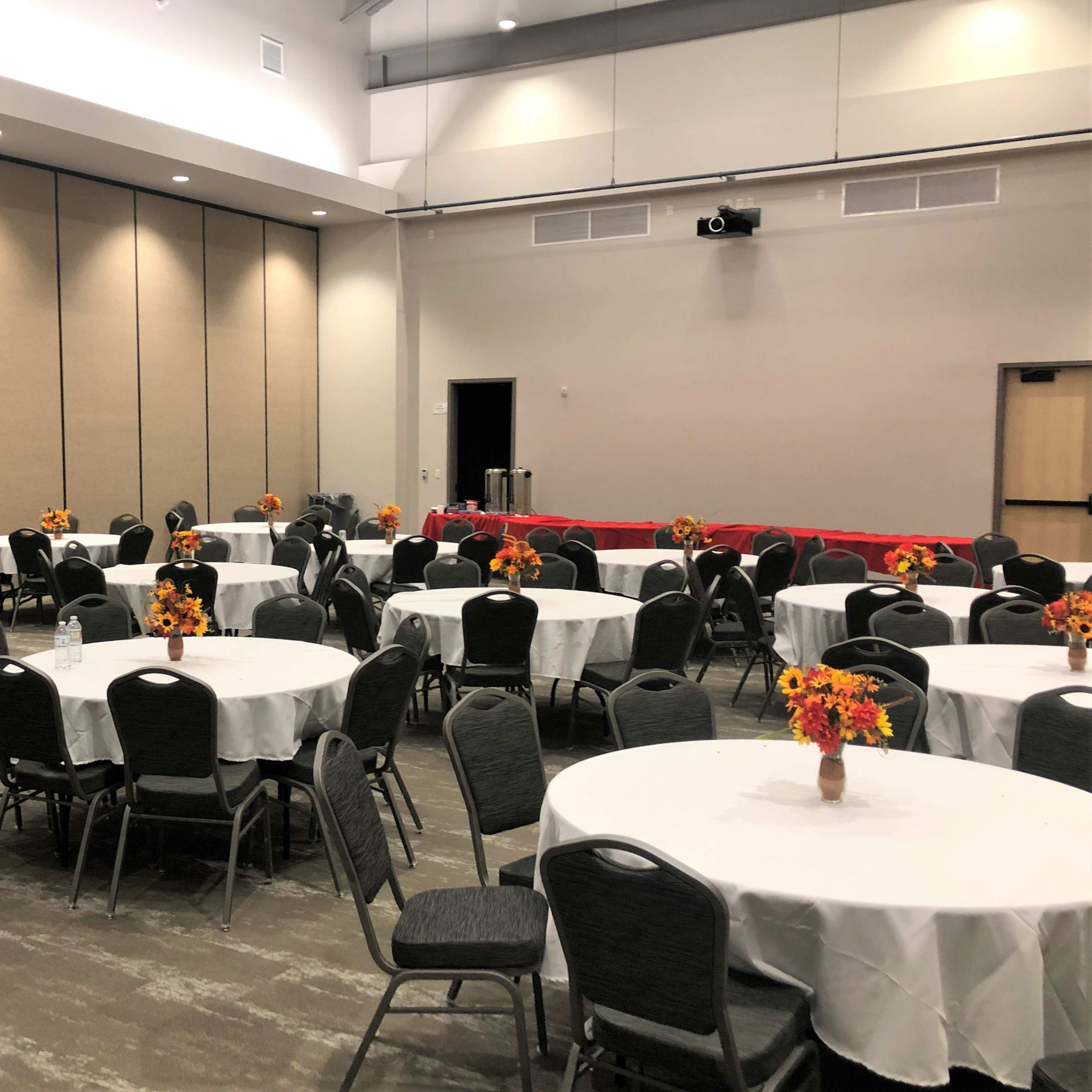 A large meeting room with round tables covered in white tablecloths and decorated with flower centerpieces, arranged in a grid pattern.