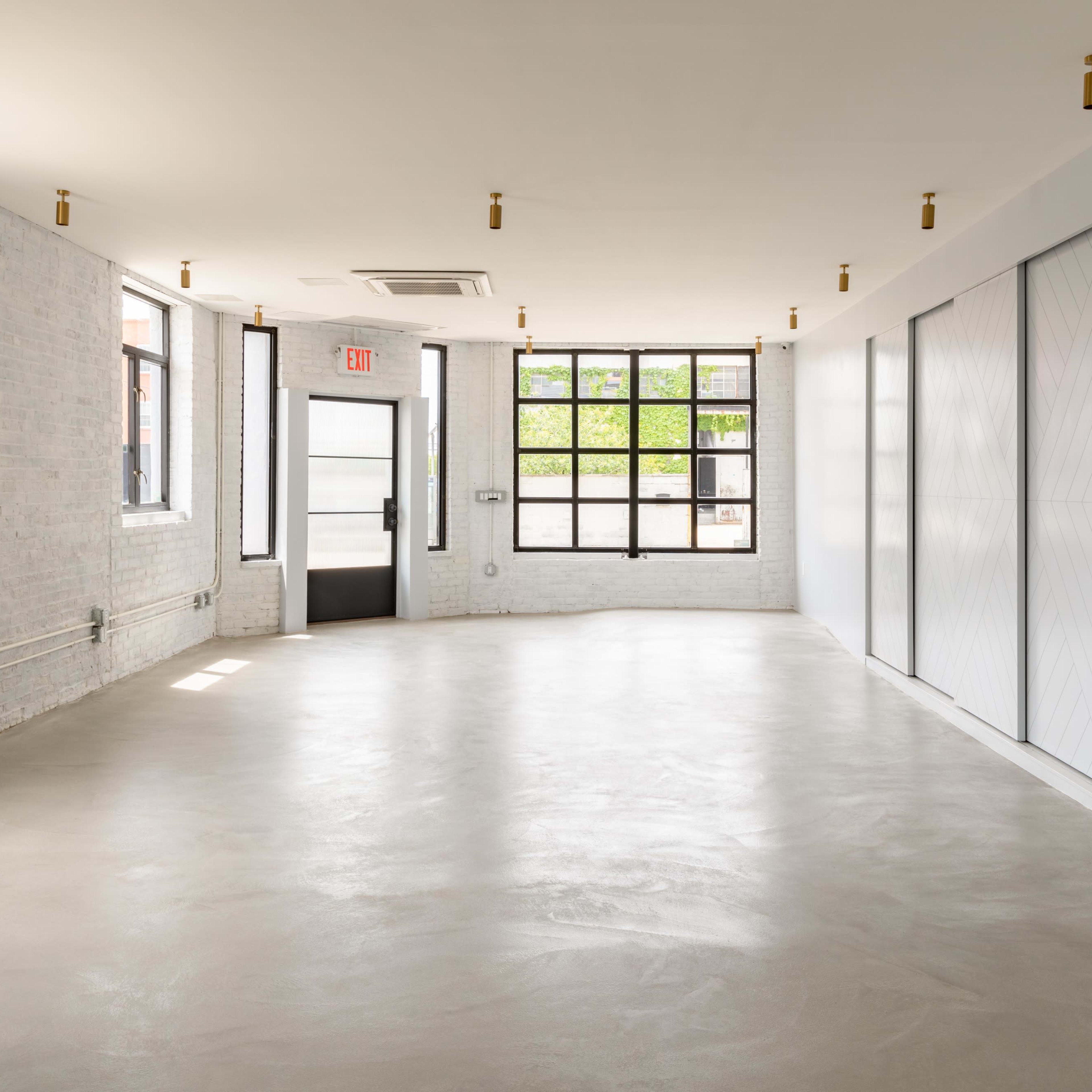 An empty room with white brick walls, large windows, and a smooth concrete floor.