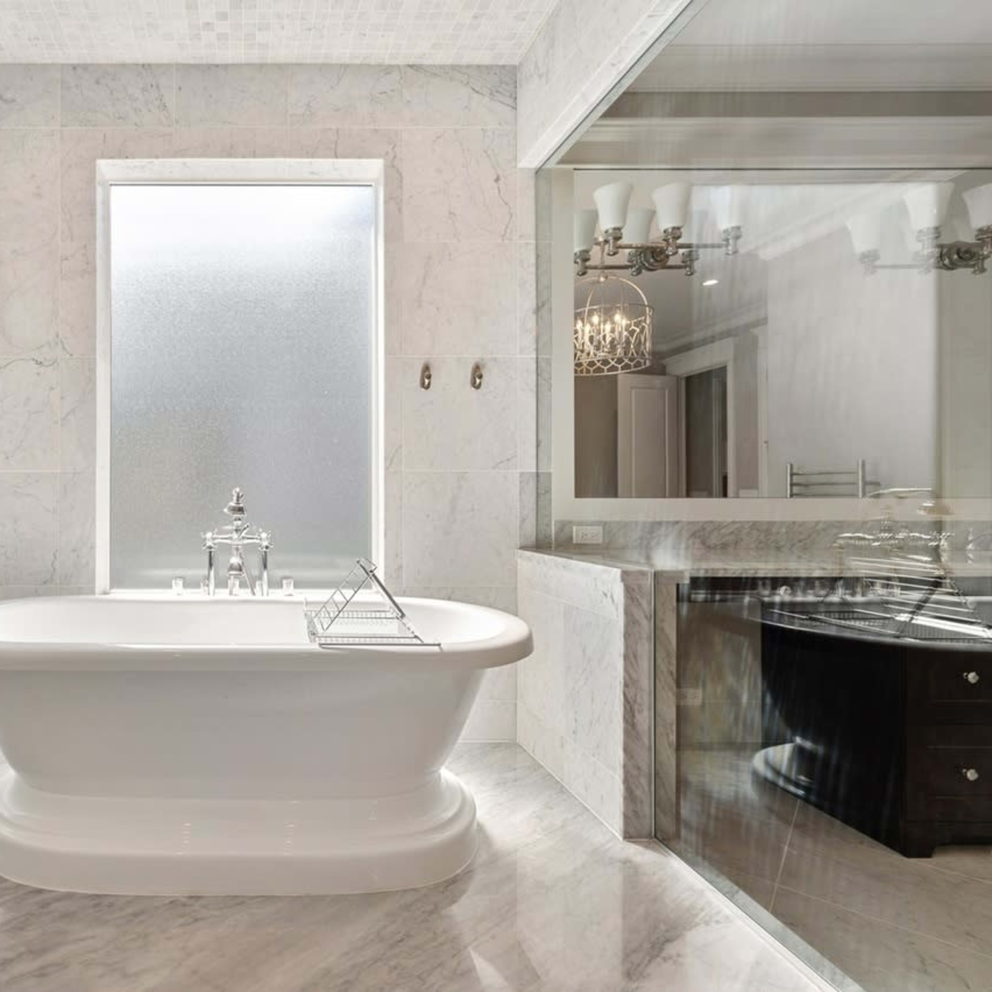 A modern bathroom featuring a freestanding white bathtub, marble walls, and a large window with frosted glass.