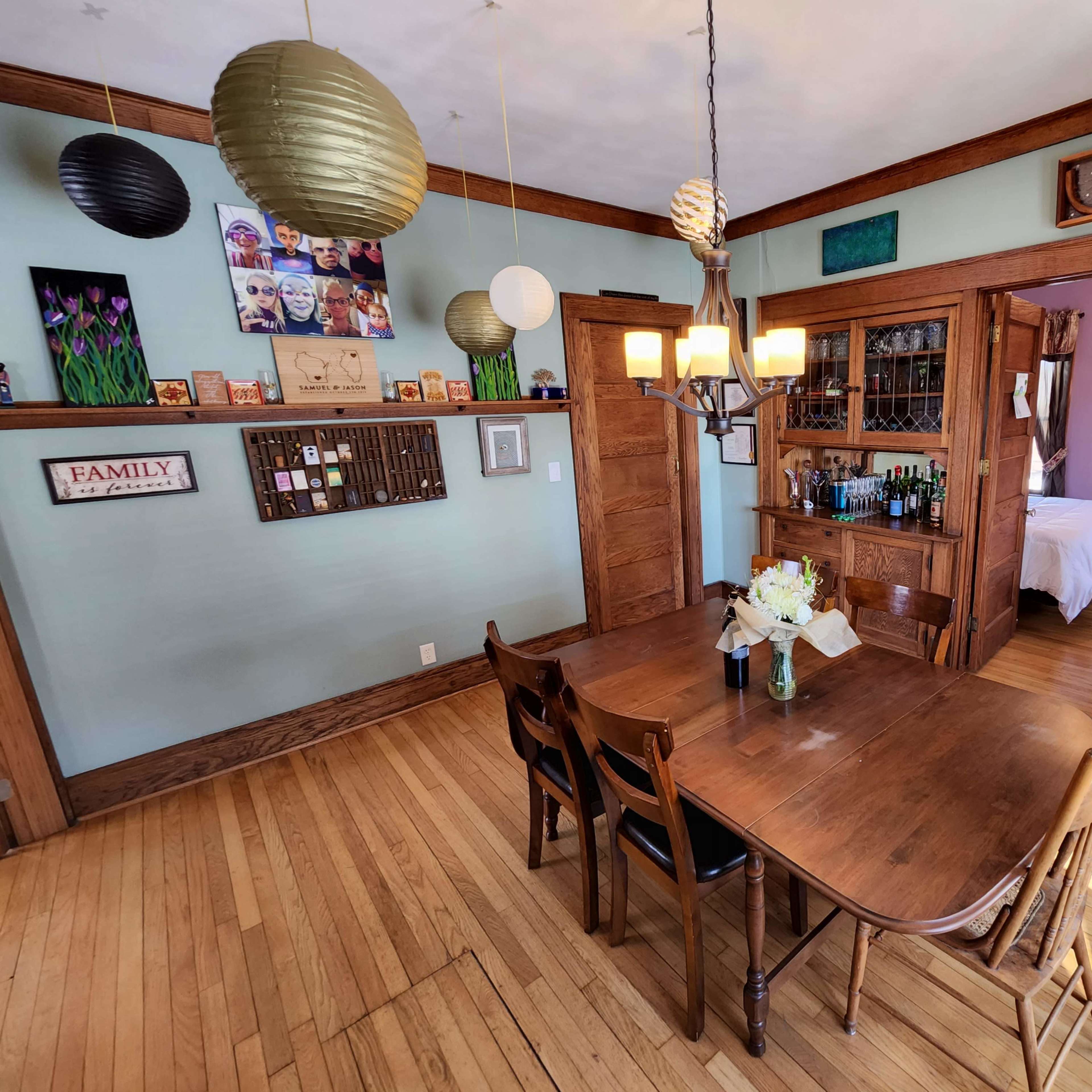 A wooden dining table with six chairs is positioned in a room featuring light blue walls and various decorative elements, including hanging lanterns and framed artwork.