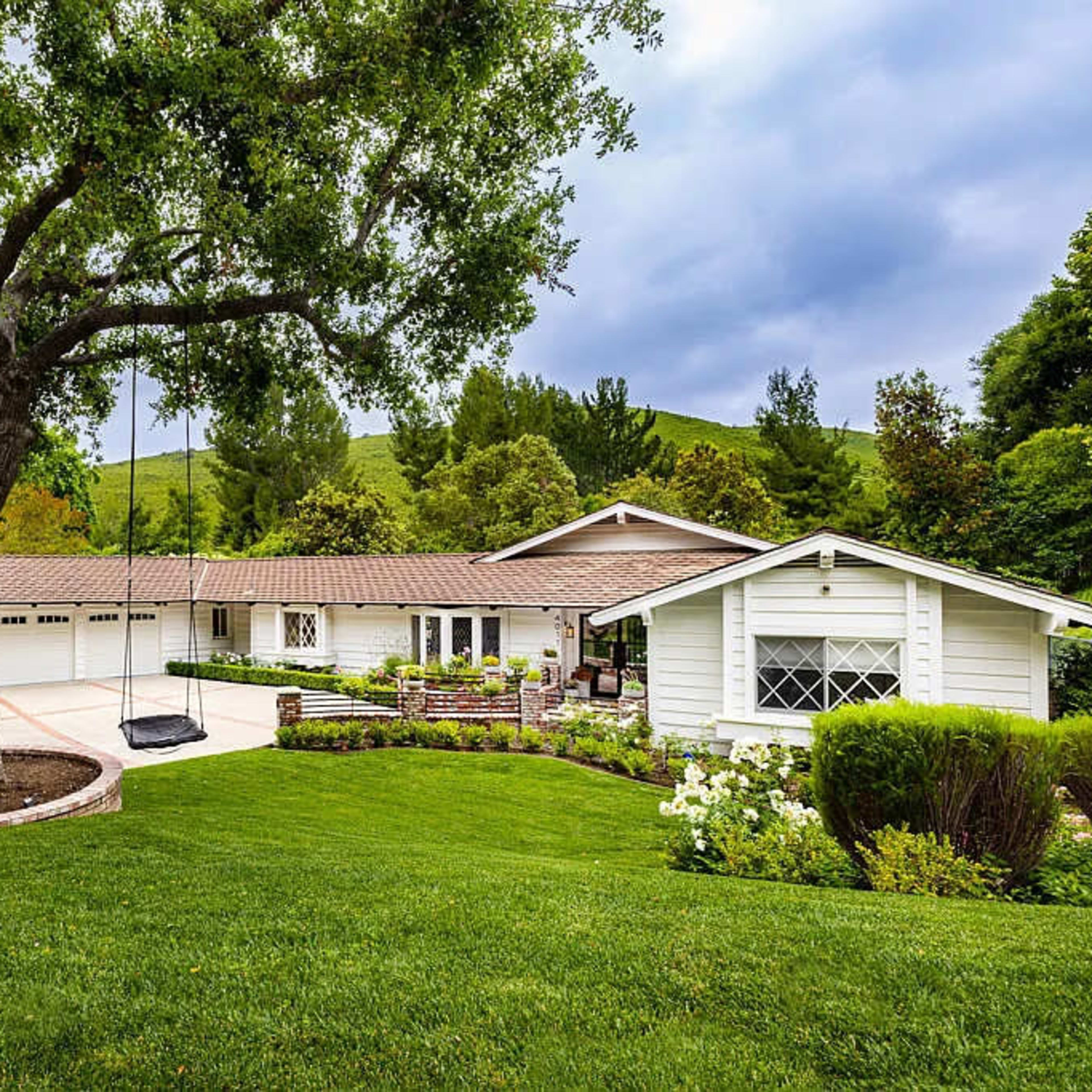 A modern single-story house is situated on a landscaped lawn with a large tree and a swing in front.