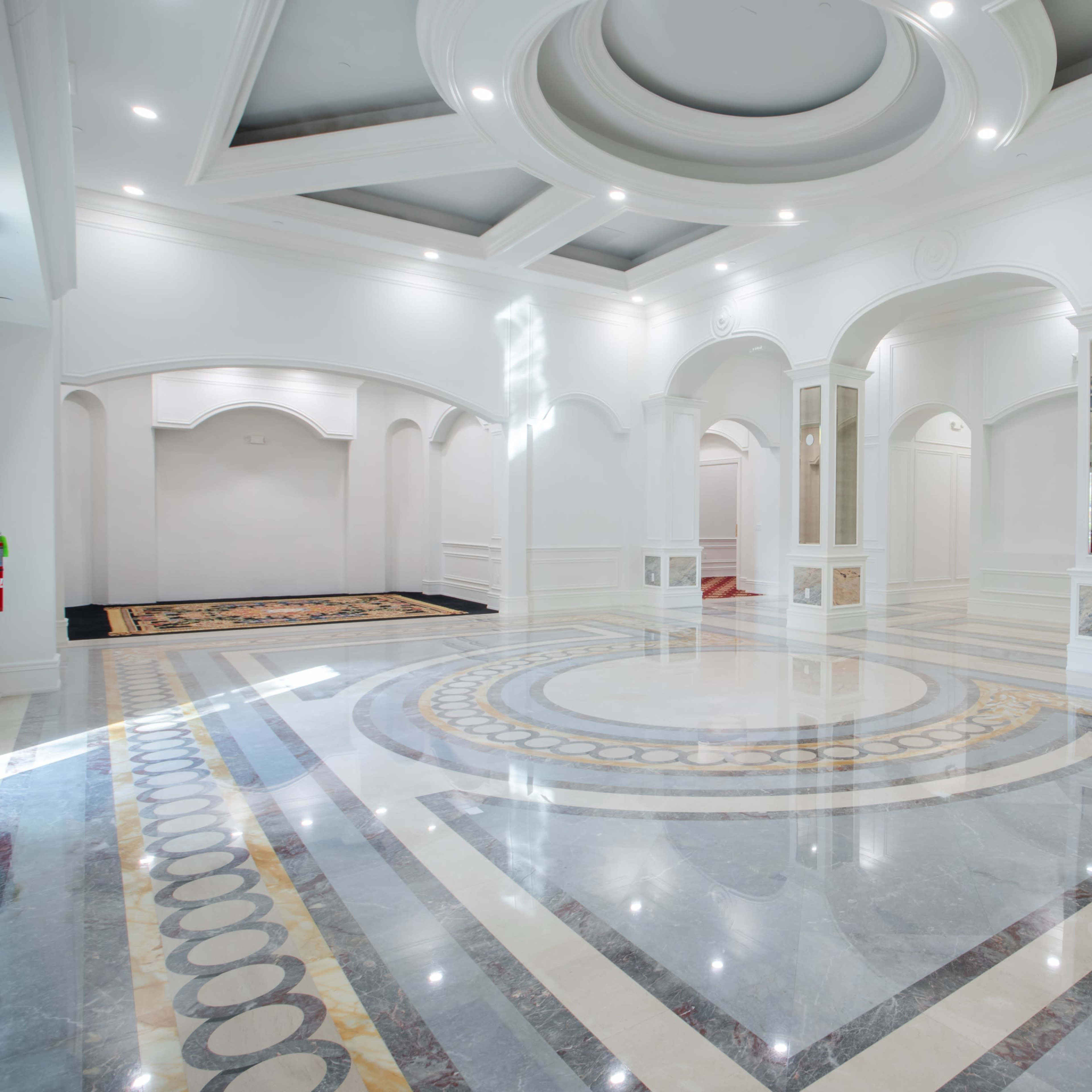 A spacious, elegantly designed interior with a polished marble floor featuring circular patterns and several archways.
