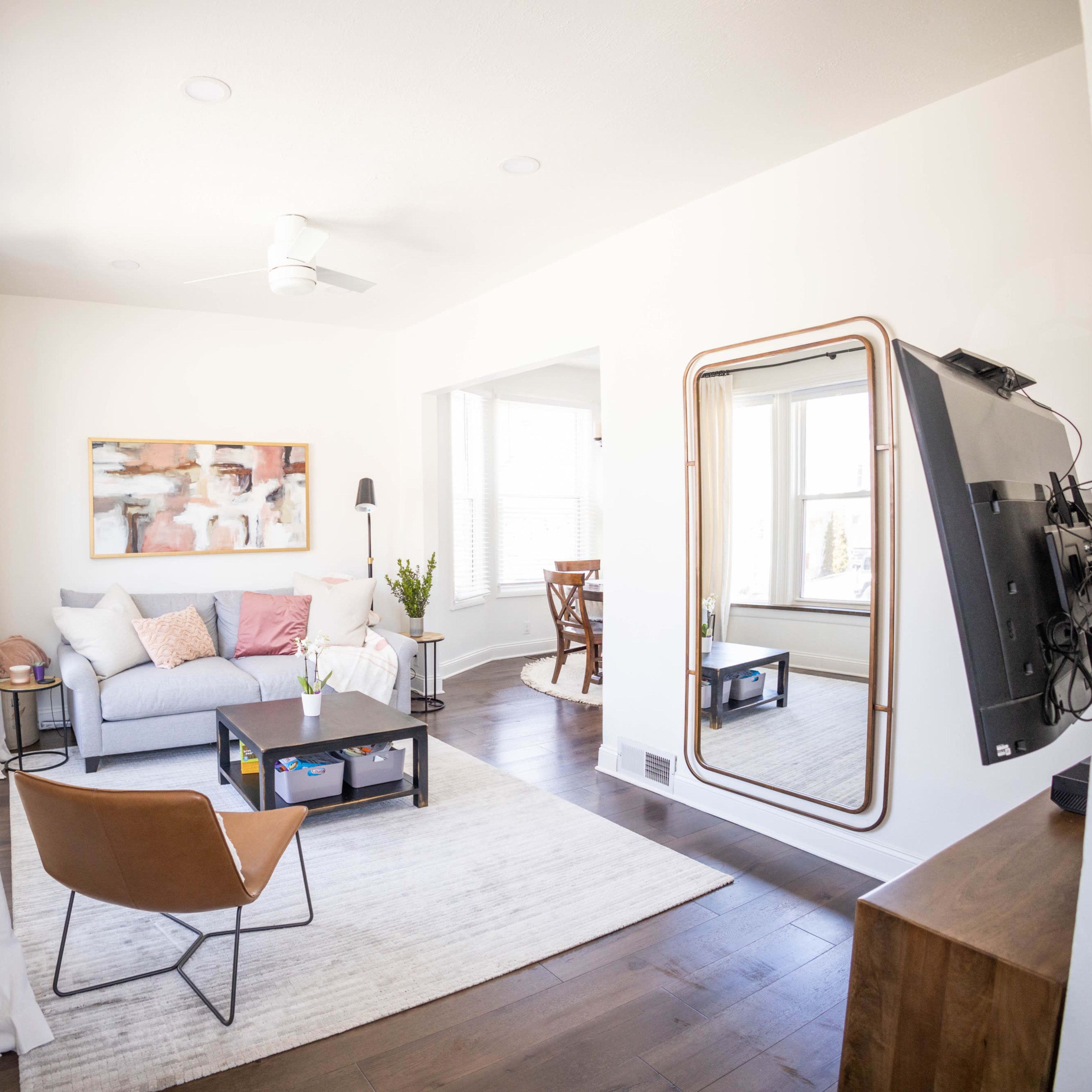 A bright living room with a gray sofa, a coffee table, a large mirror, and a mounted television.