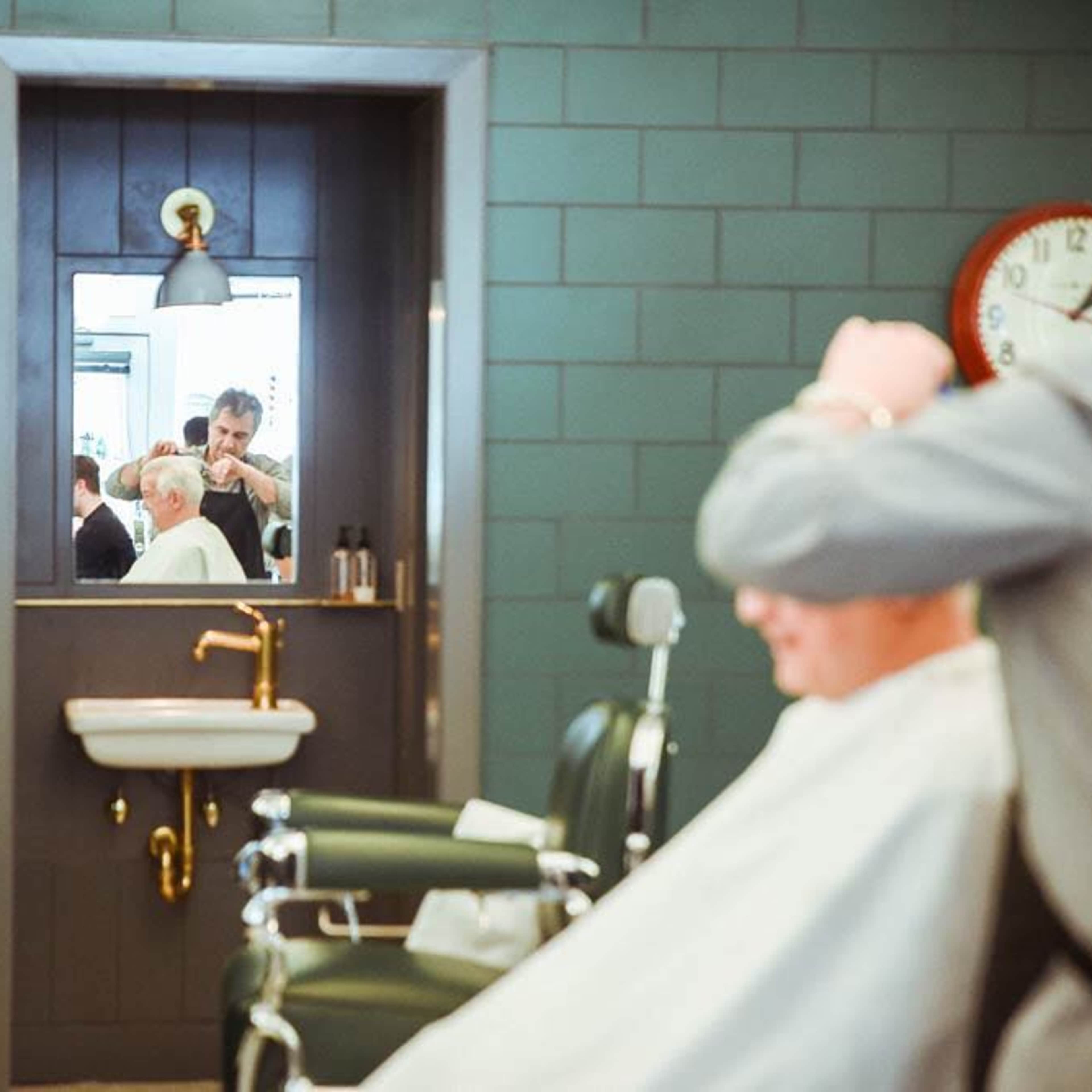 A barber is cutting a man's hair in front of a mirror in a vintage-style barbershop.