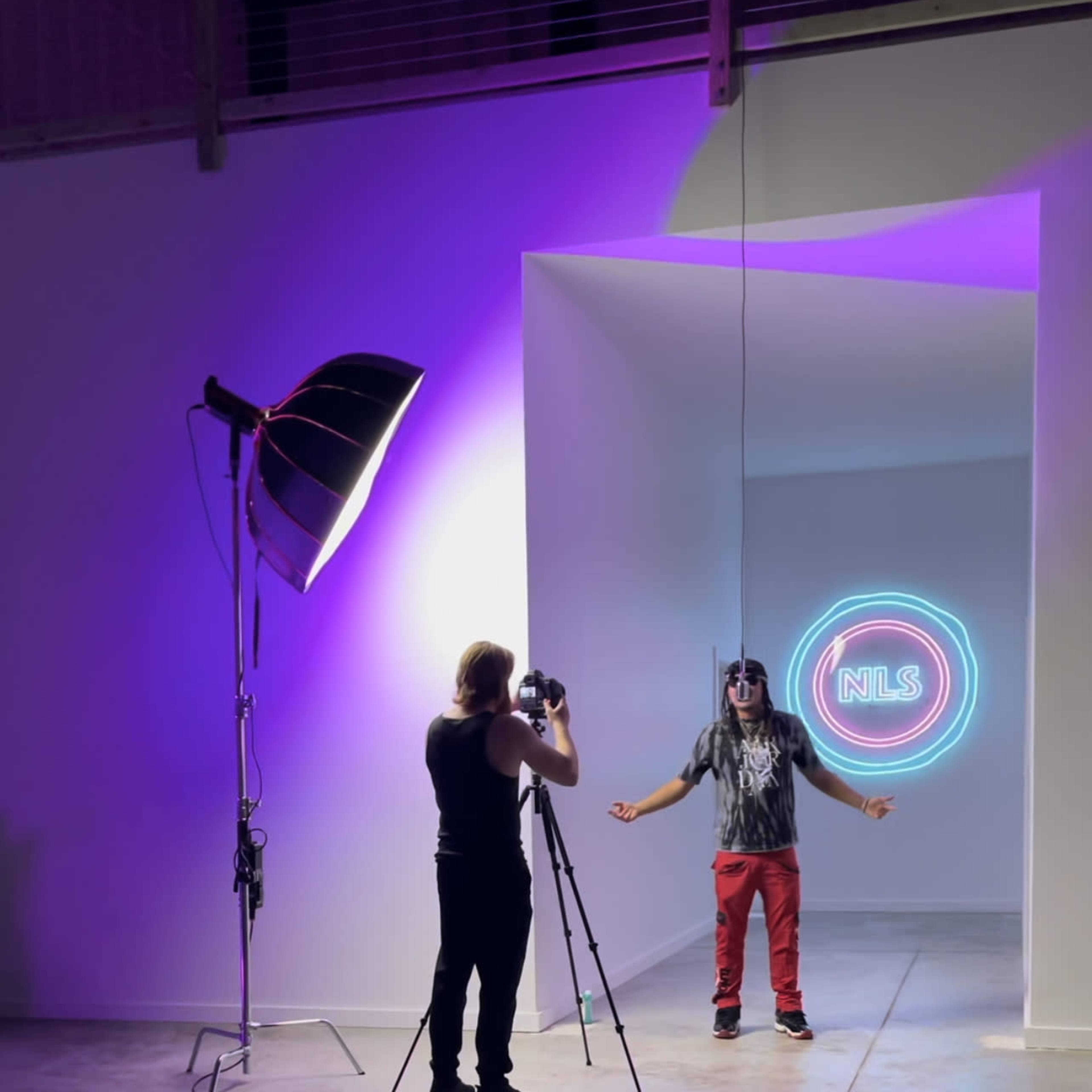 A photographer captures a model standing in a brightly lit studio with a neon sign in the background.