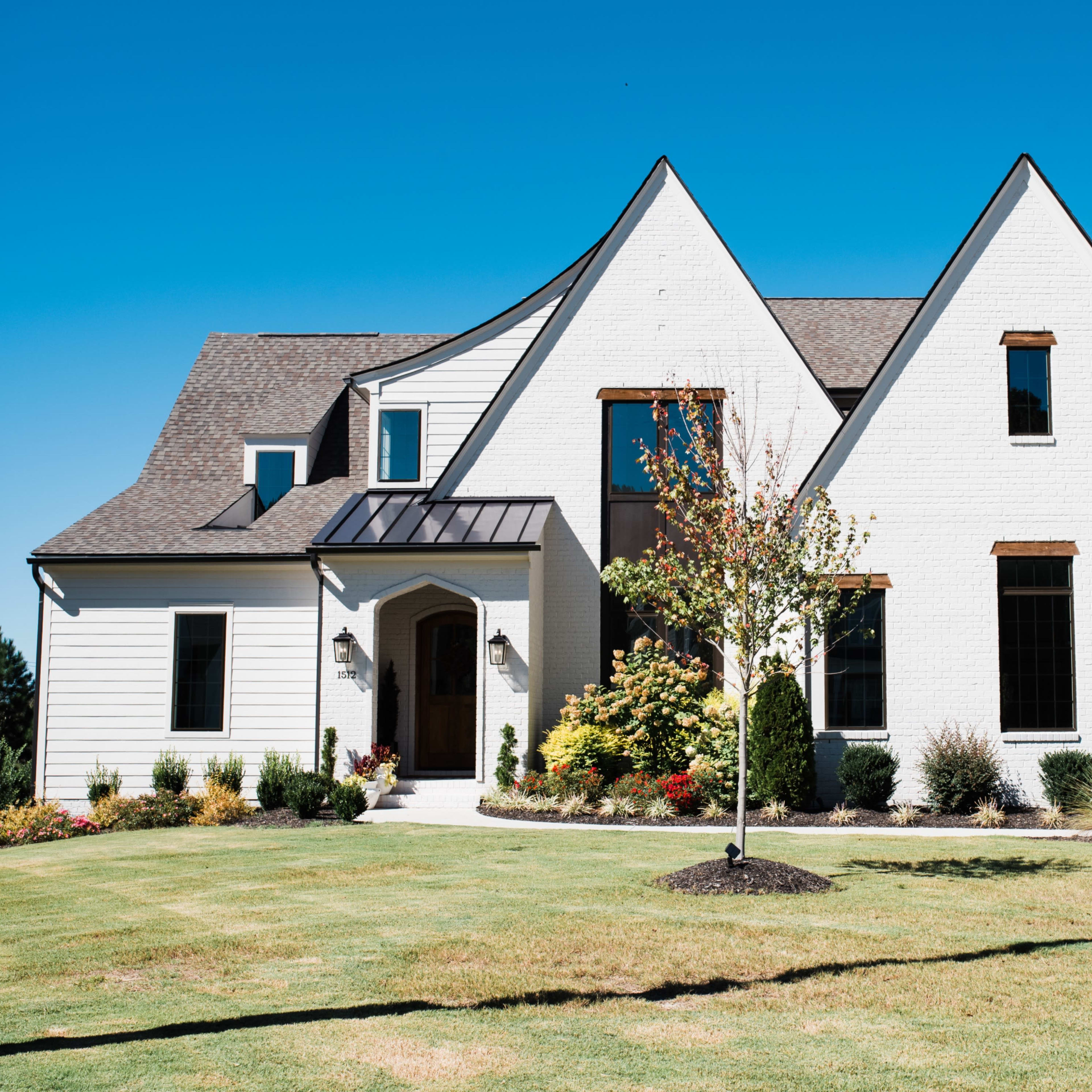 A modern two-story home features a mix of white brick and siding with a landscaped front yard and a prominent entrance.