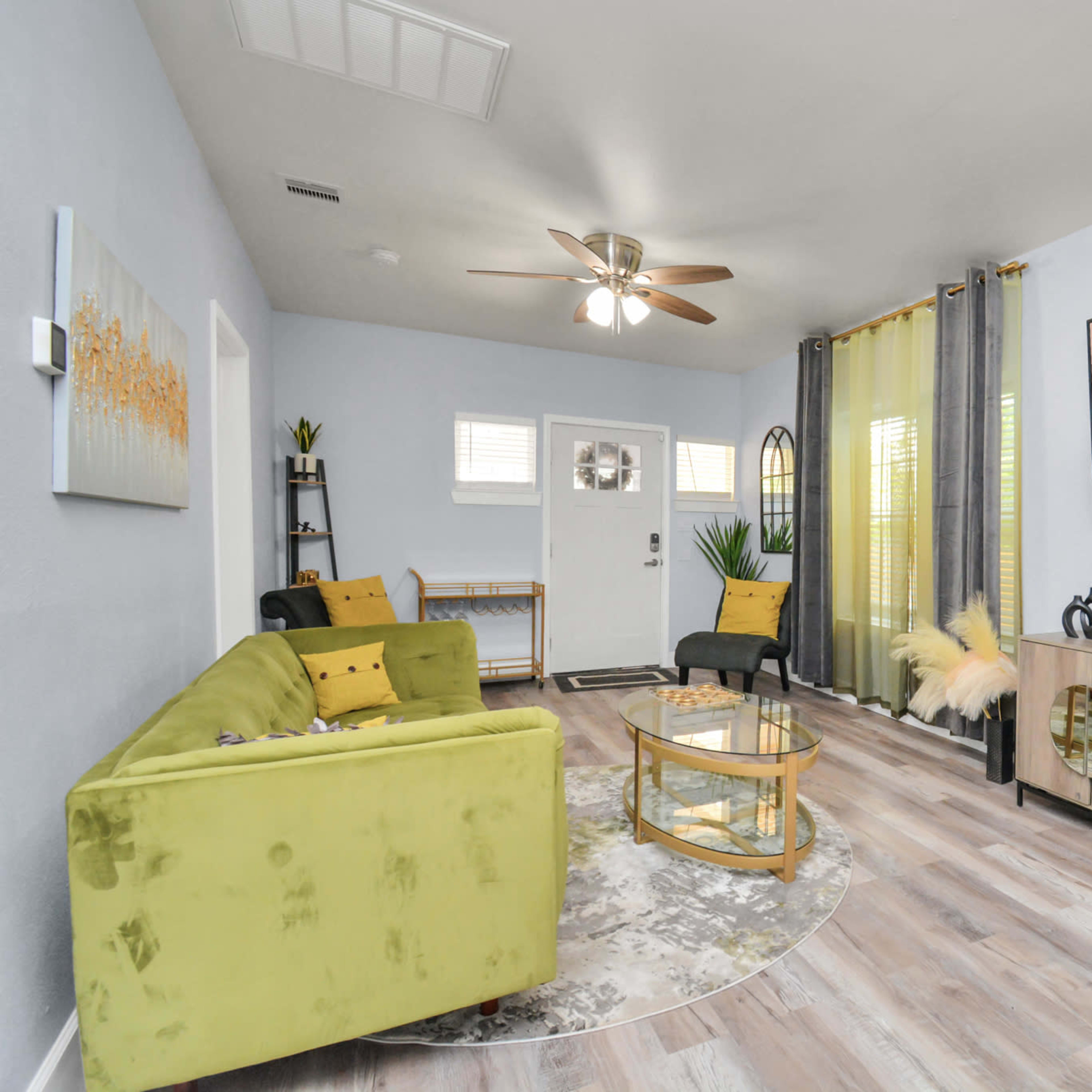A modern living room with a green sofa, a round coffee table, a television mounted on the wall, and large windows with curtains.