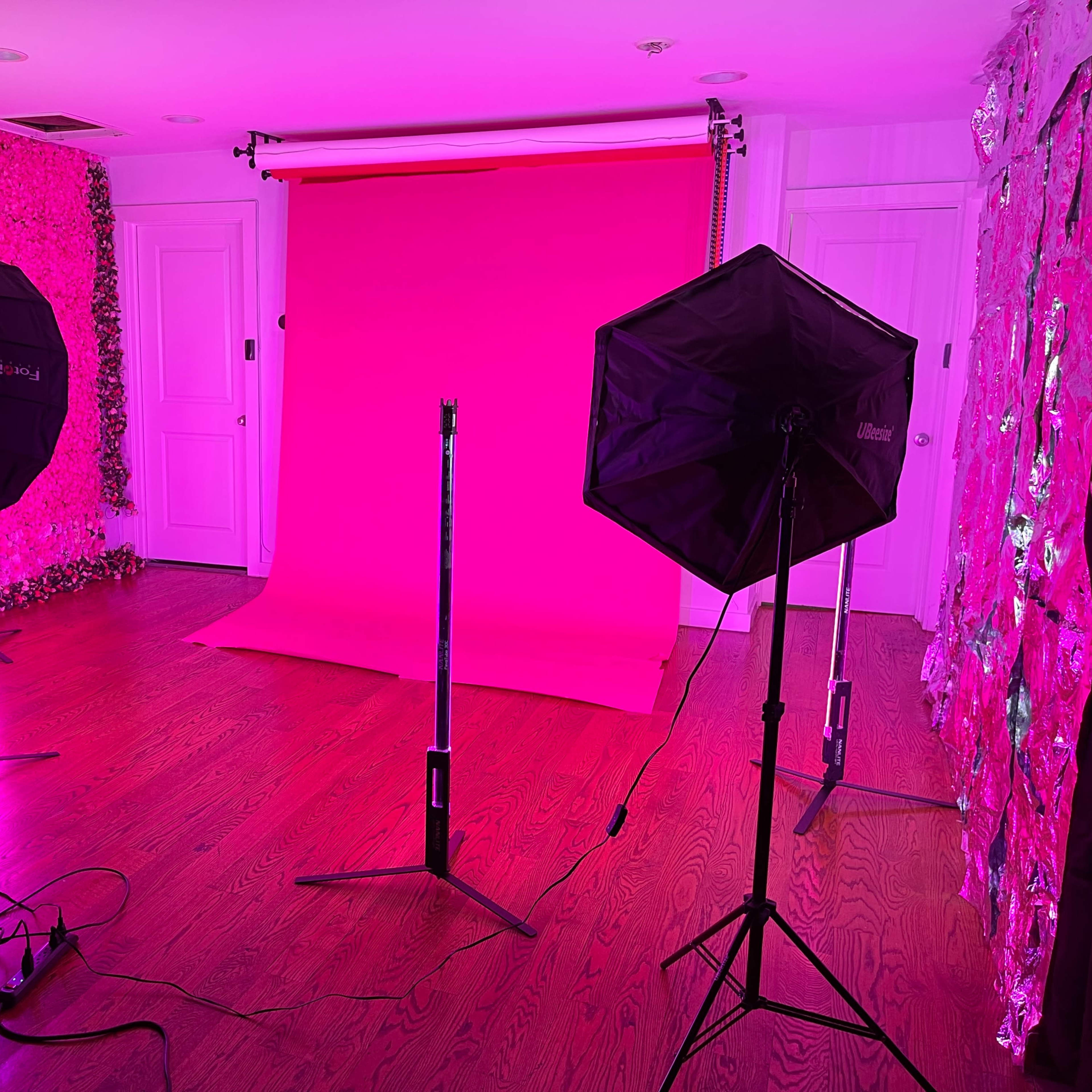 A photography studio with pink backdrop, illuminated by two studio lights on either side.