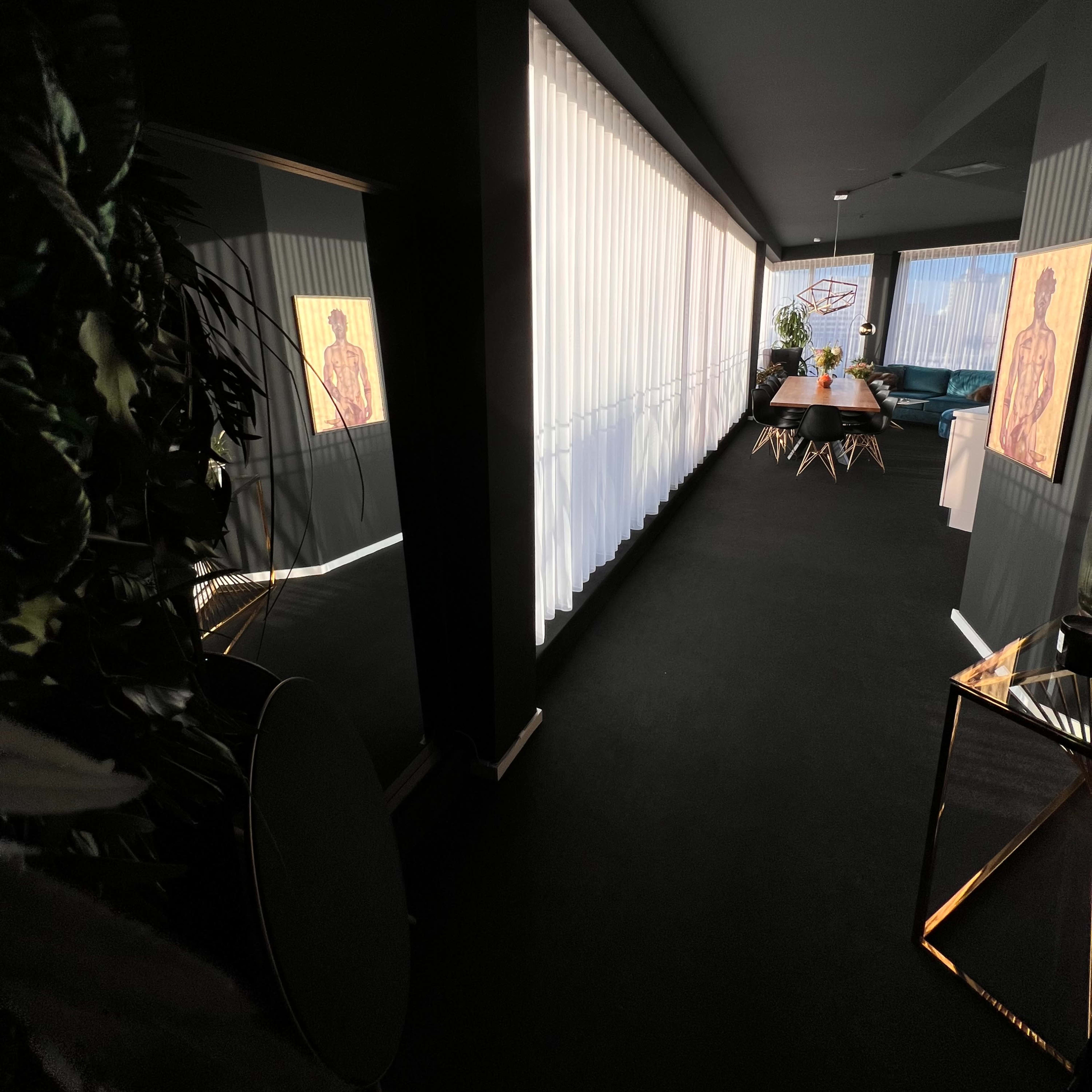 A modern hallway leading to a dining area, with natural light filtering in through sheer curtains and art pieces displayed on the walls.