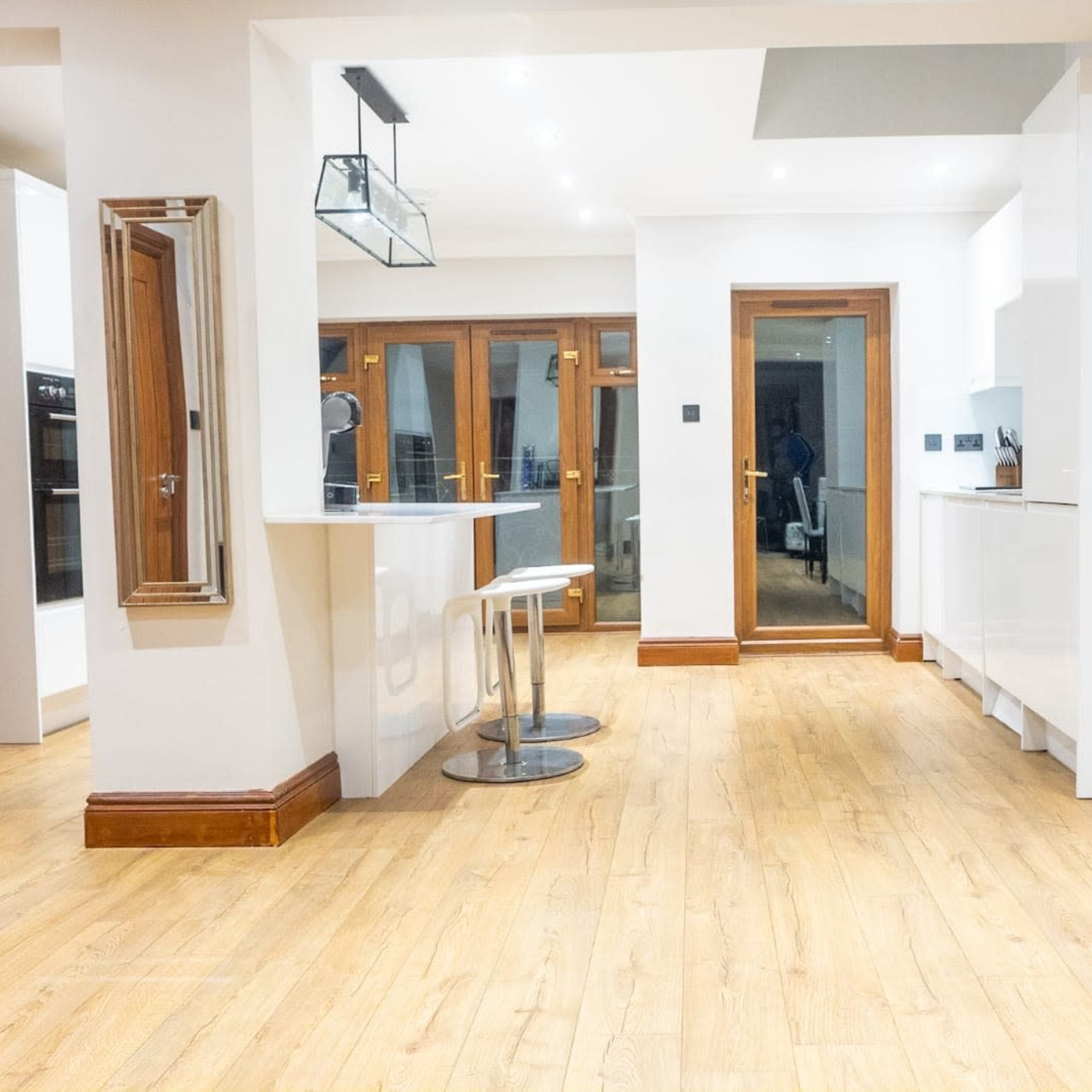 A modern kitchen area with wooden flooring, white cabinetry, and glass doors leading to an outdoor space.