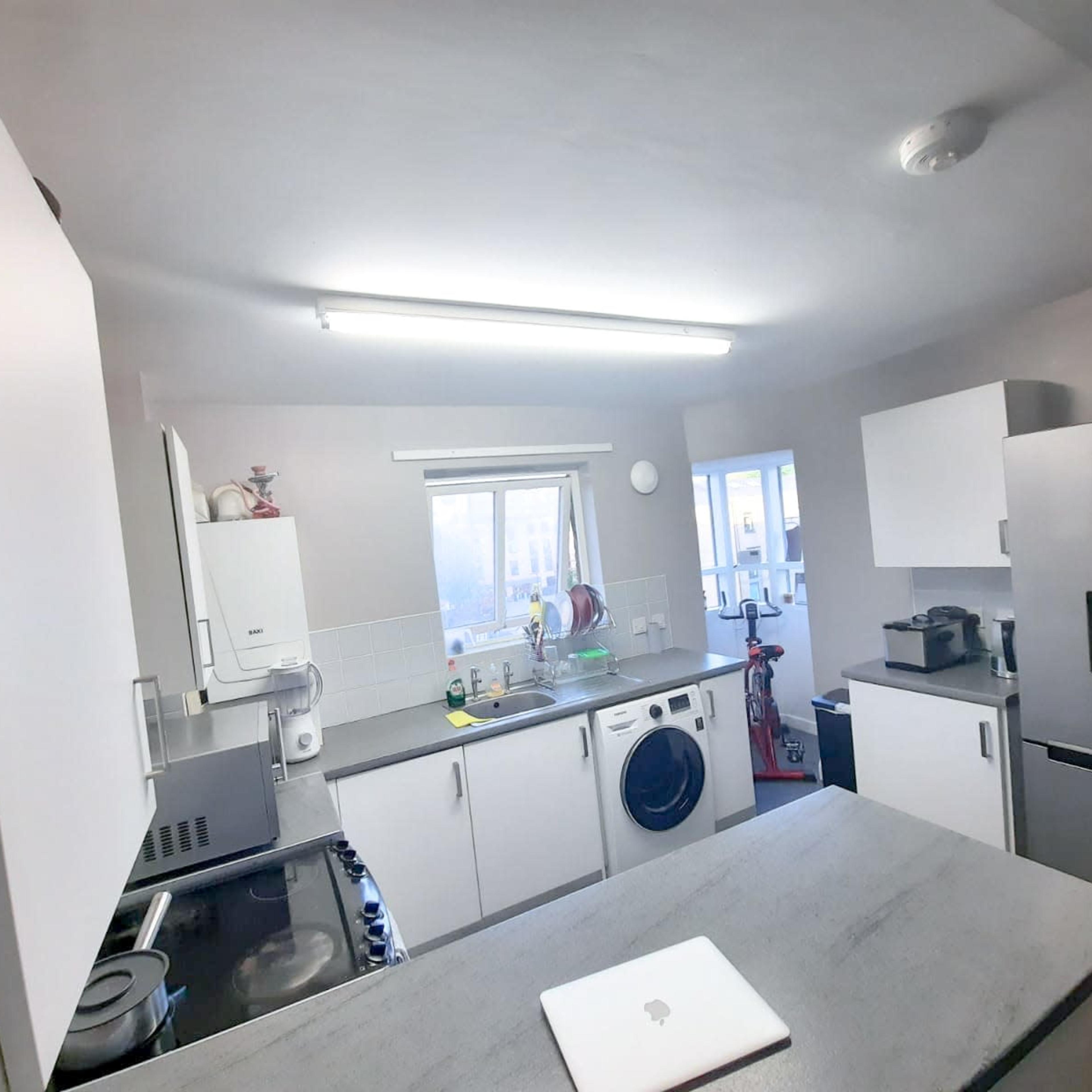 A bright, modern kitchen features white cabinets, a sink near a window, an integrated oven, and a washing machine.