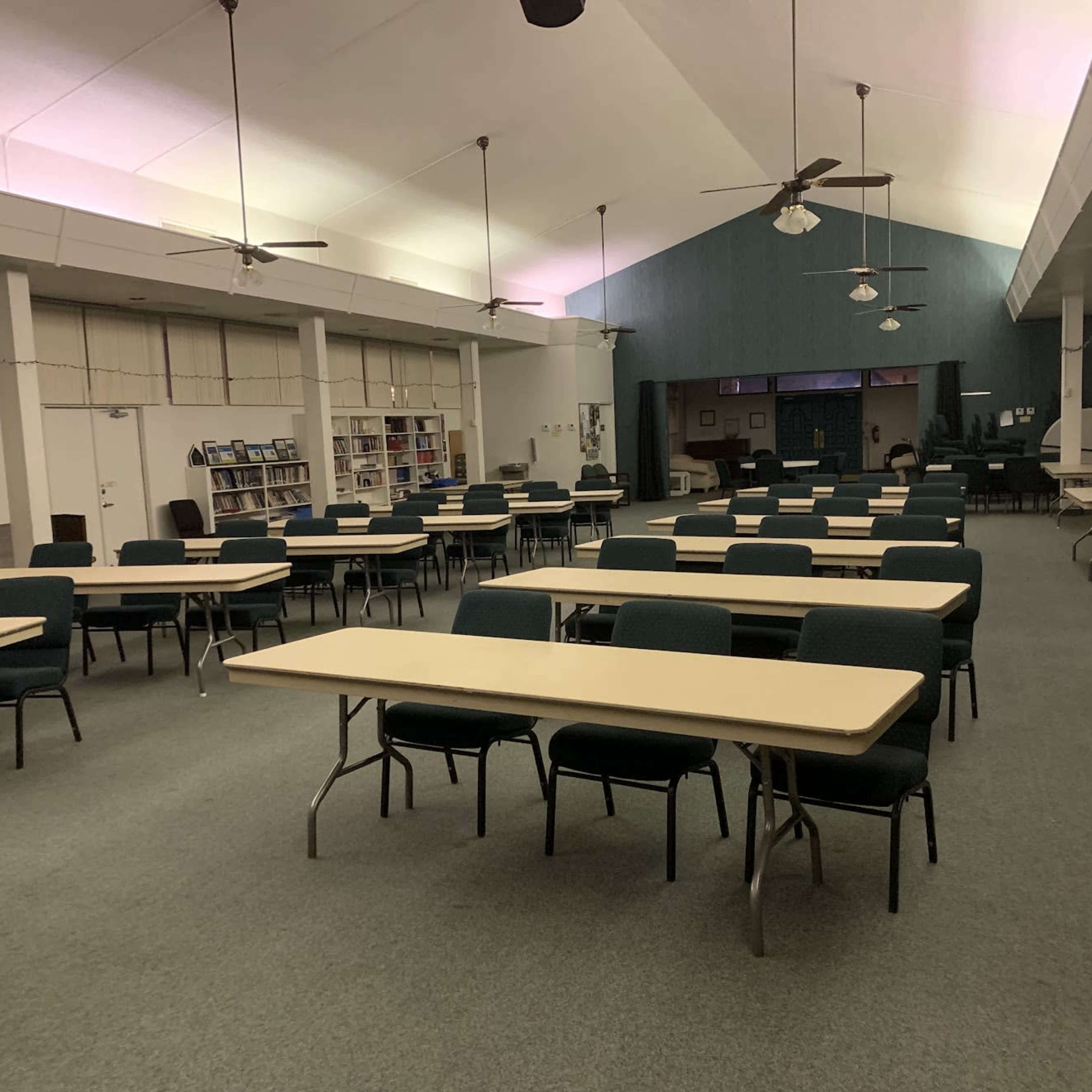 A large, empty room filled with rows of tables and chairs, with a stage area at the far end.