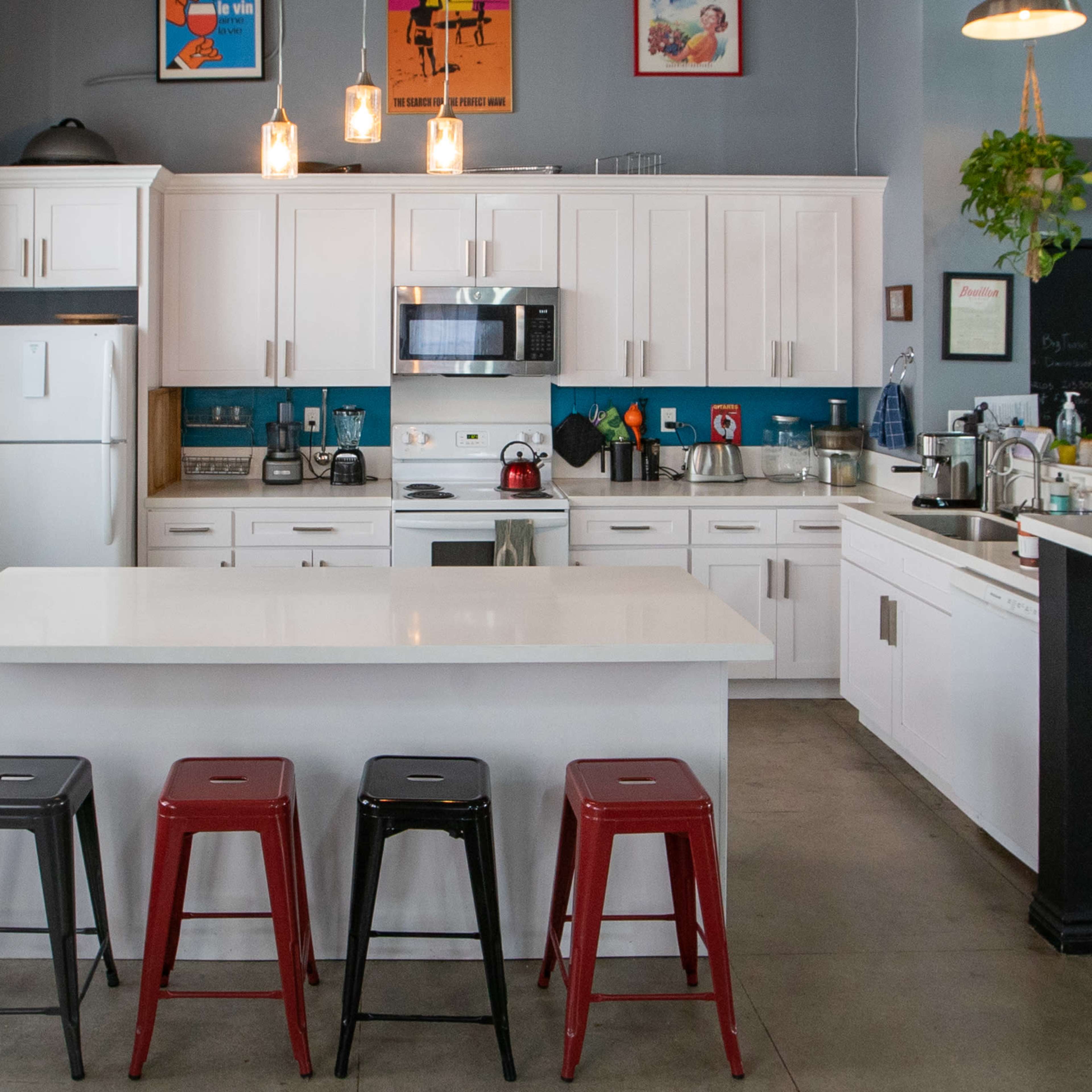 A modern kitchen with white cabinets, a central island, and four metal stools in front of it.