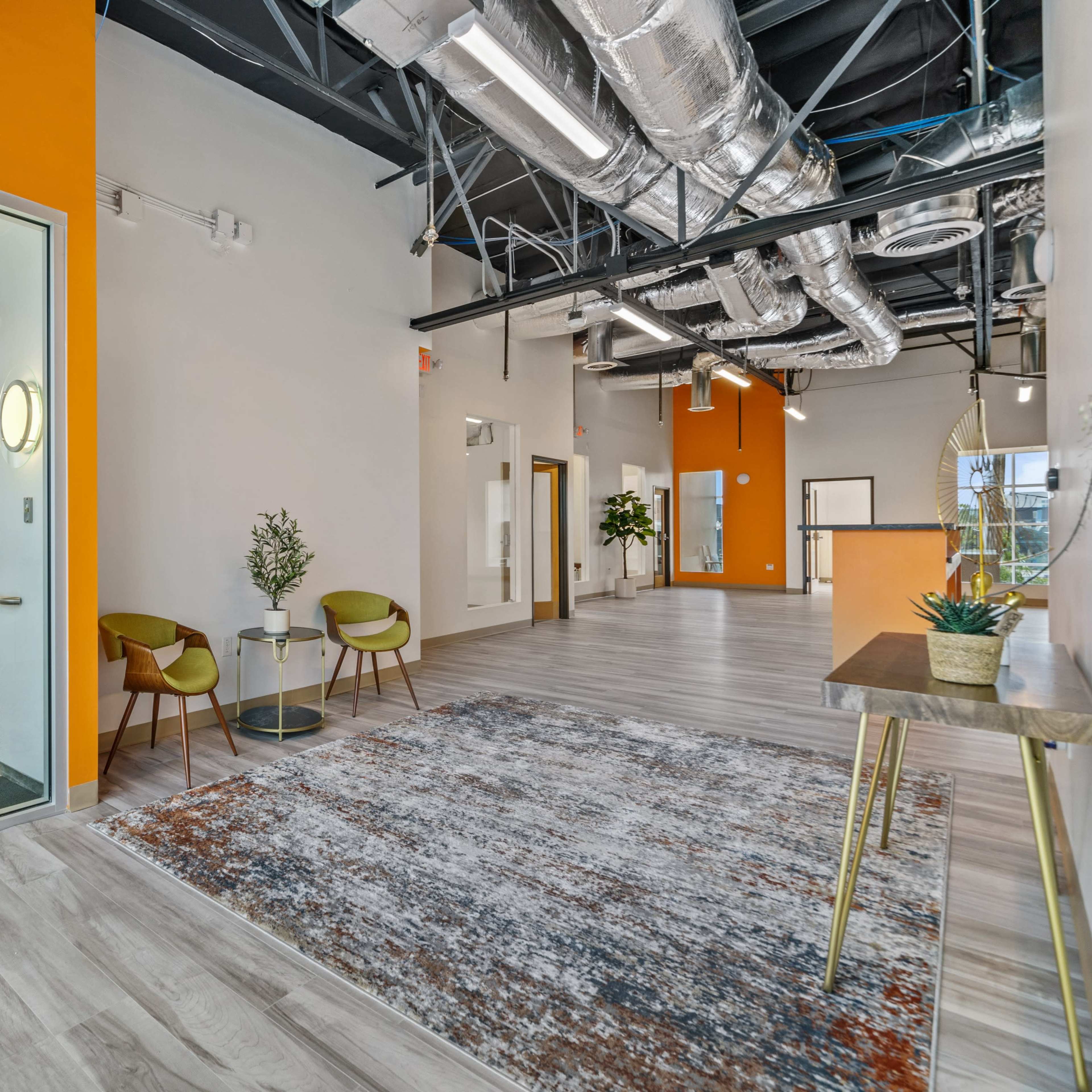 A modern interior space with orange accent walls, a seating area, and large windows allowing natural light to enter.