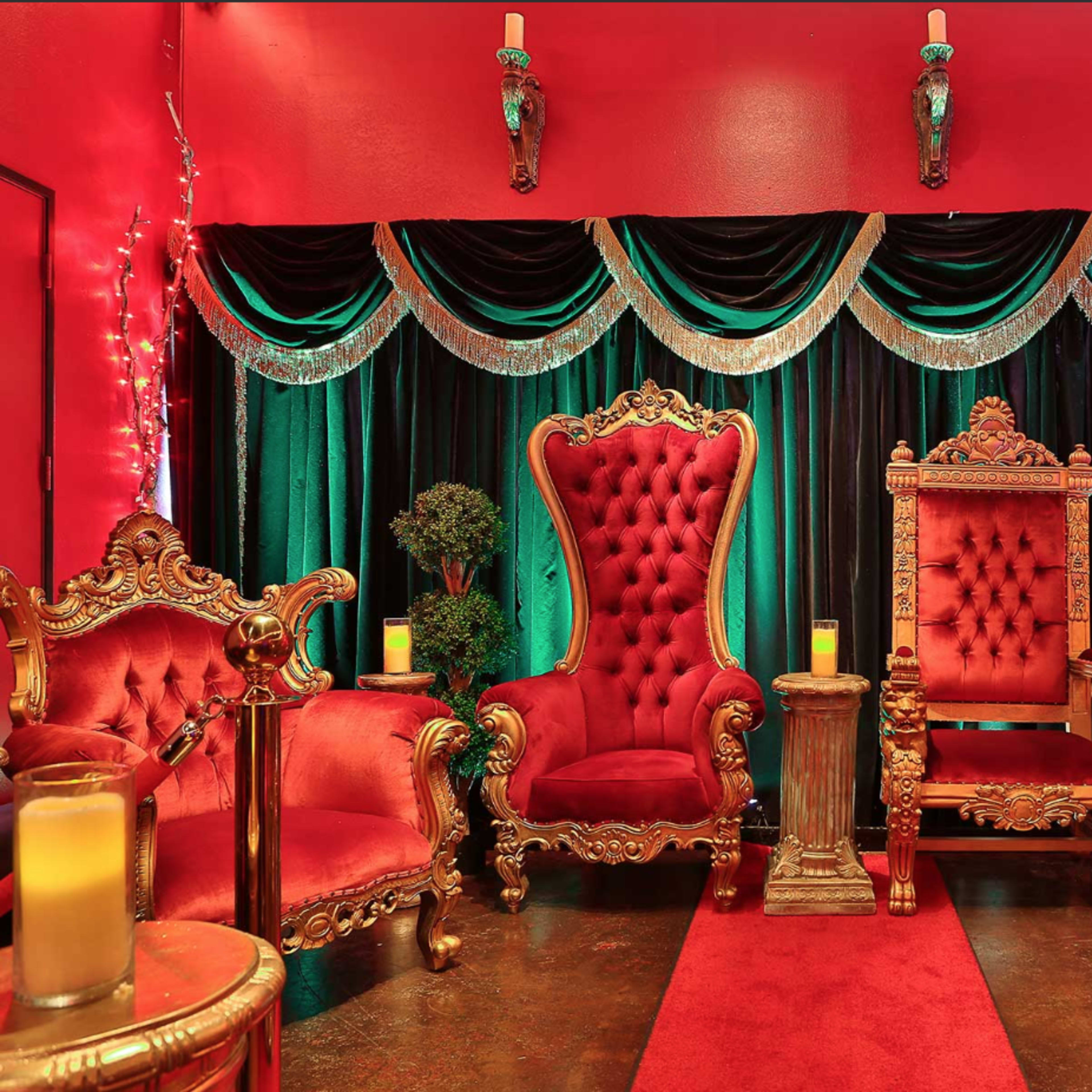 An opulent seating area with two ornate red and gold armchairs, flanked by green and black drapery and illuminated by soft candlelight.