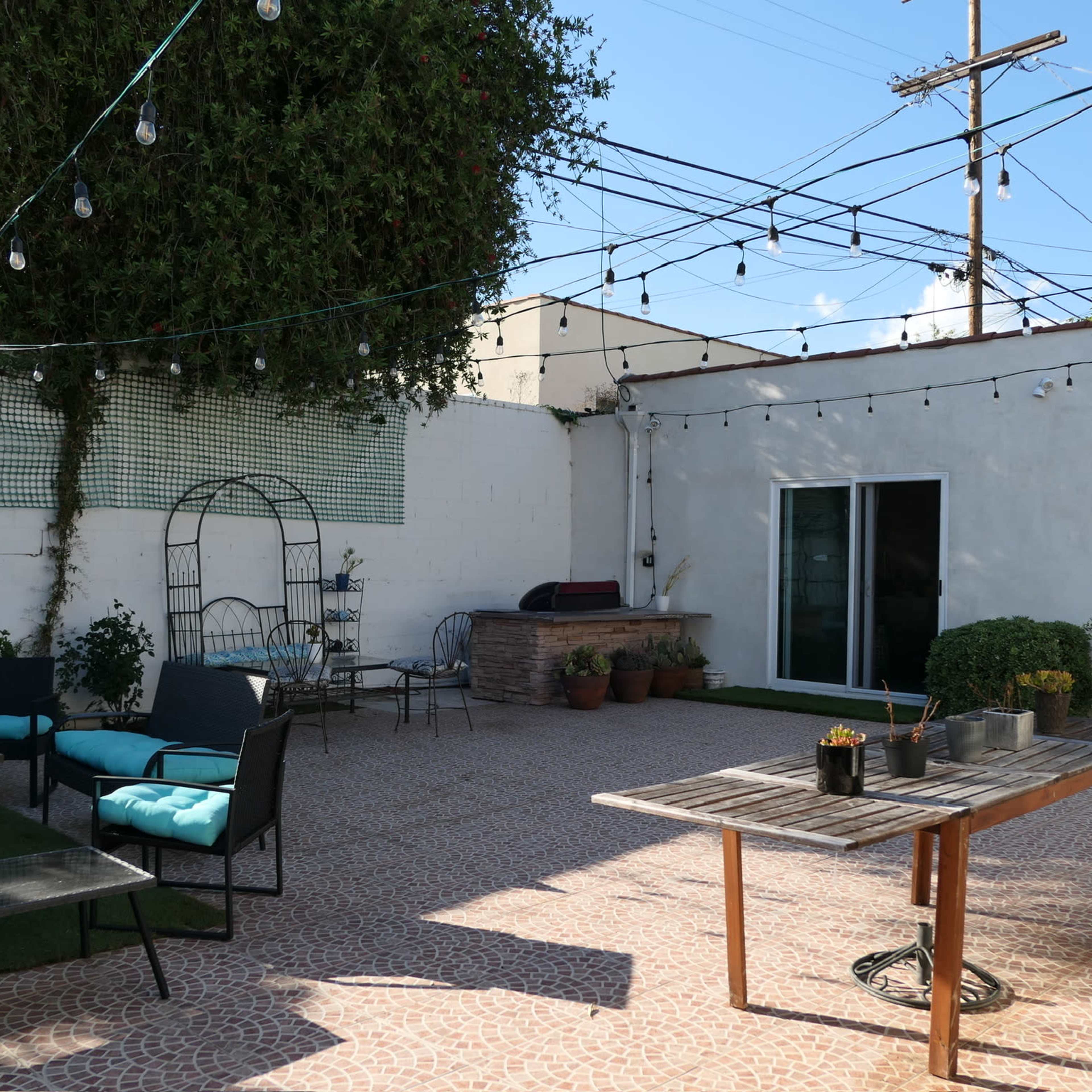 A patio area featuring outdoor seating, a table, and string lights, with a wall and garage in the background.