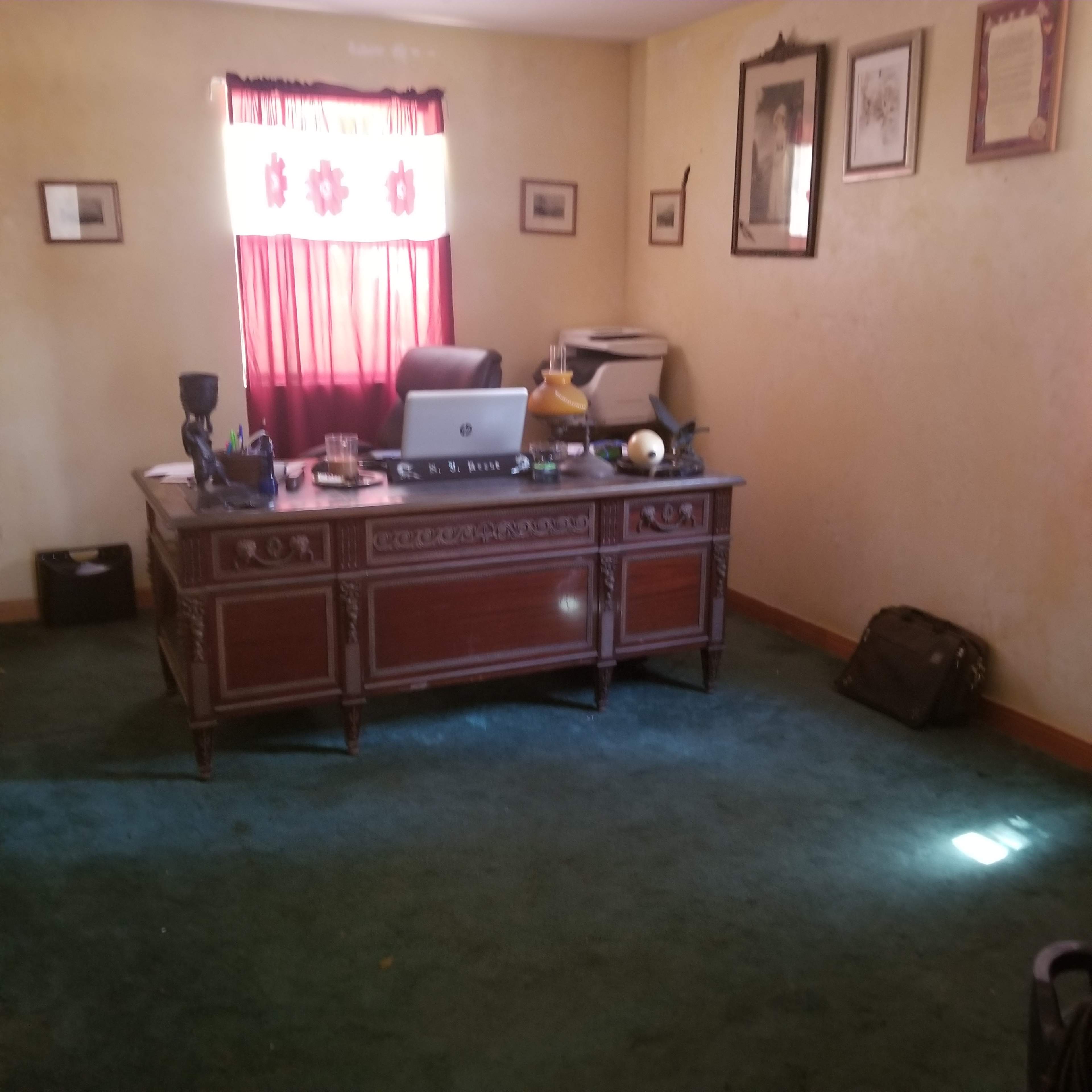 An office with a wooden desk, a computer, and a chair, surrounded by decorated walls and a window covered by a red curtain.