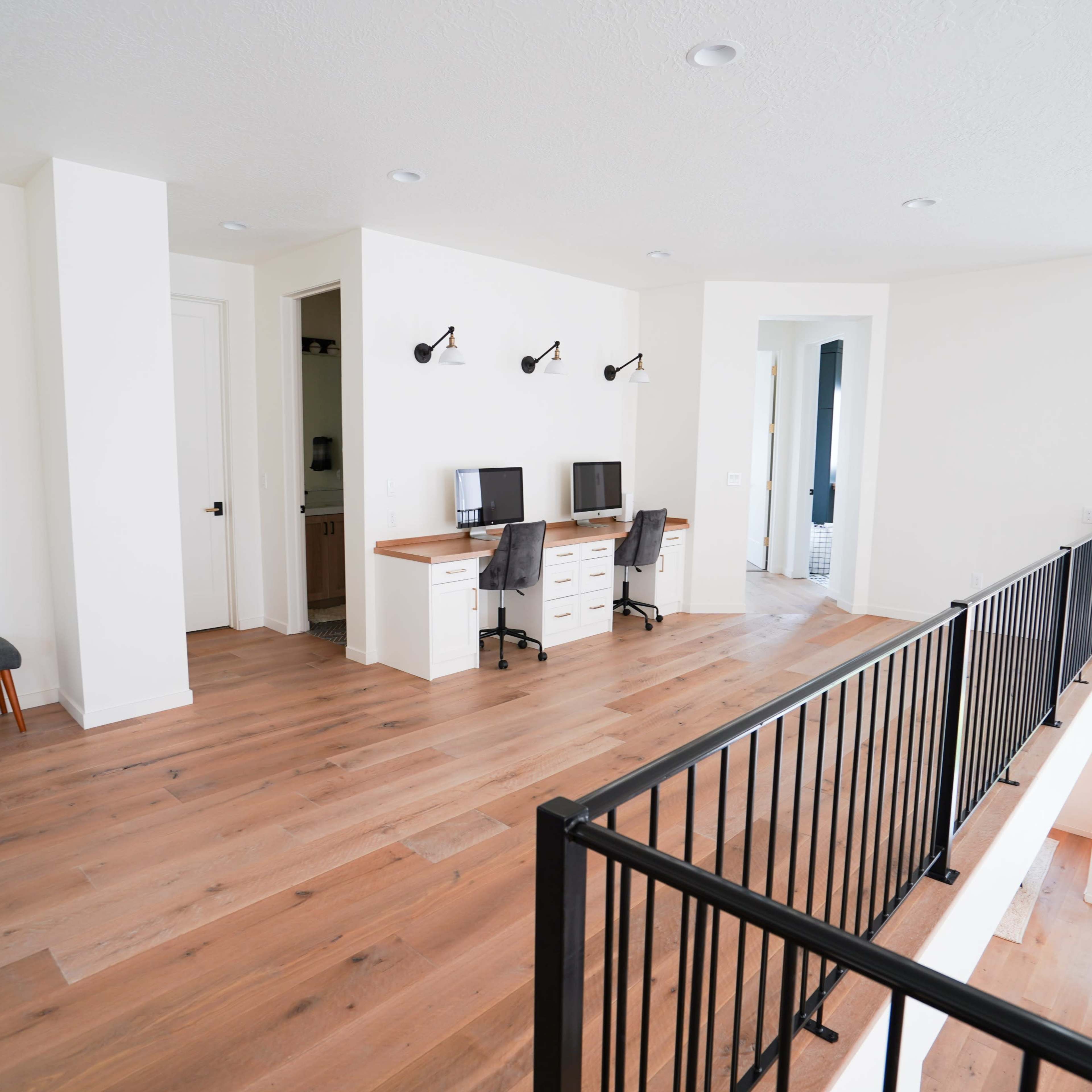 A modern open space with two workstations, a bench, and a circular mirror, all featuring light-colored walls and wooden flooring.