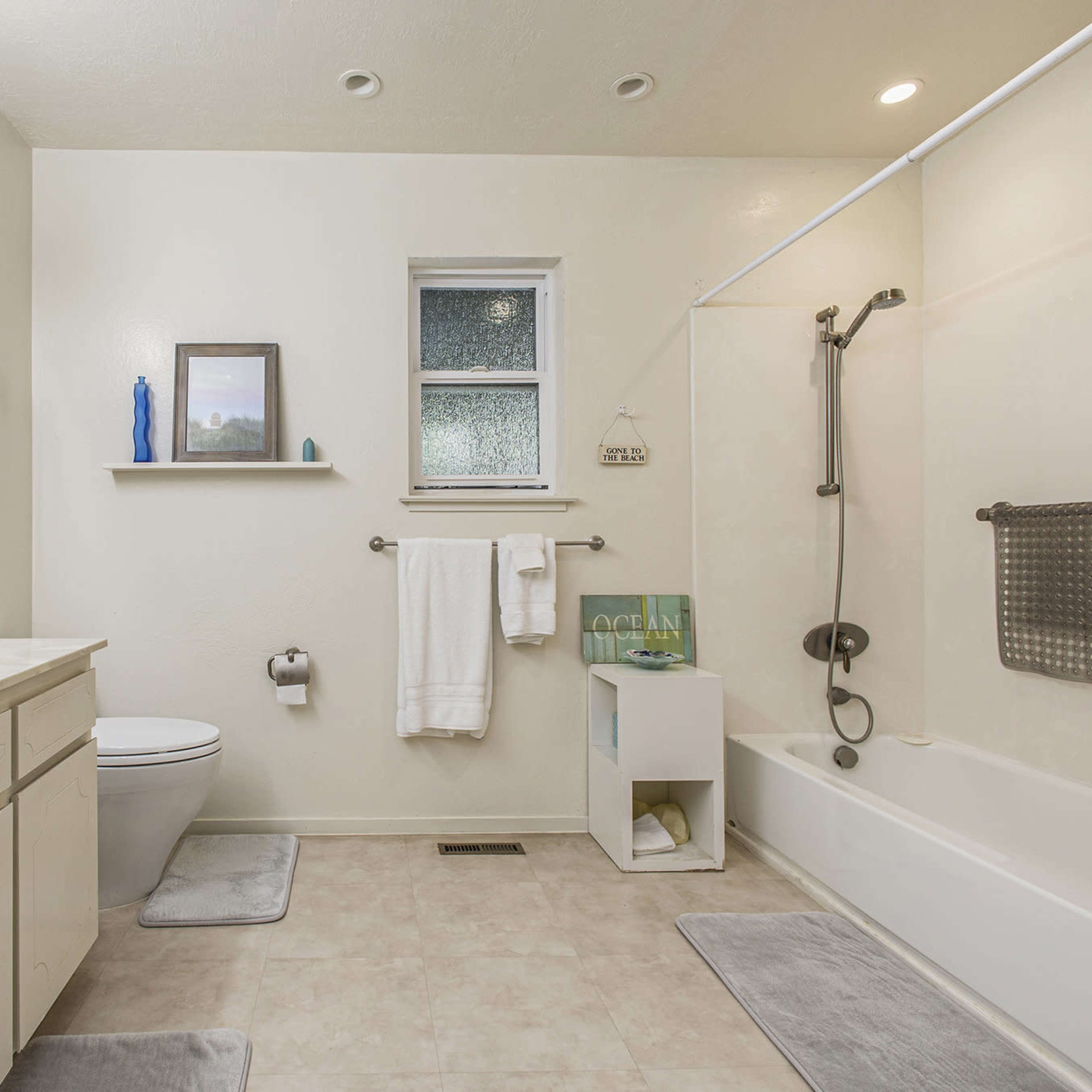 A clean bathroom with a bathtub, toilet, sink, and mirrors, featuring light-colored walls and neutral-toned flooring.