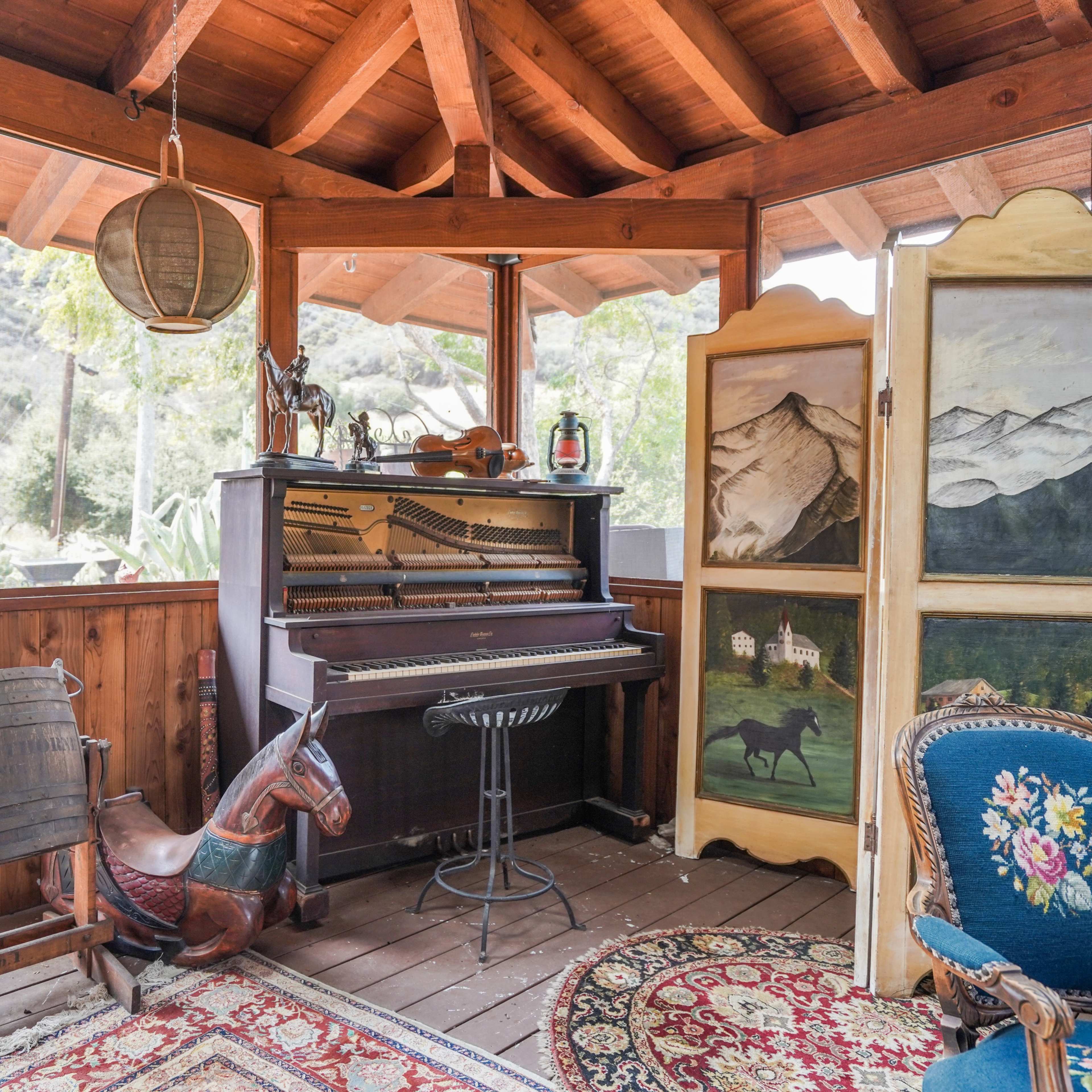 A rustic interior with a vintage piano, a rocking horse, and a decorative folding screen featuring mountain landscapes.