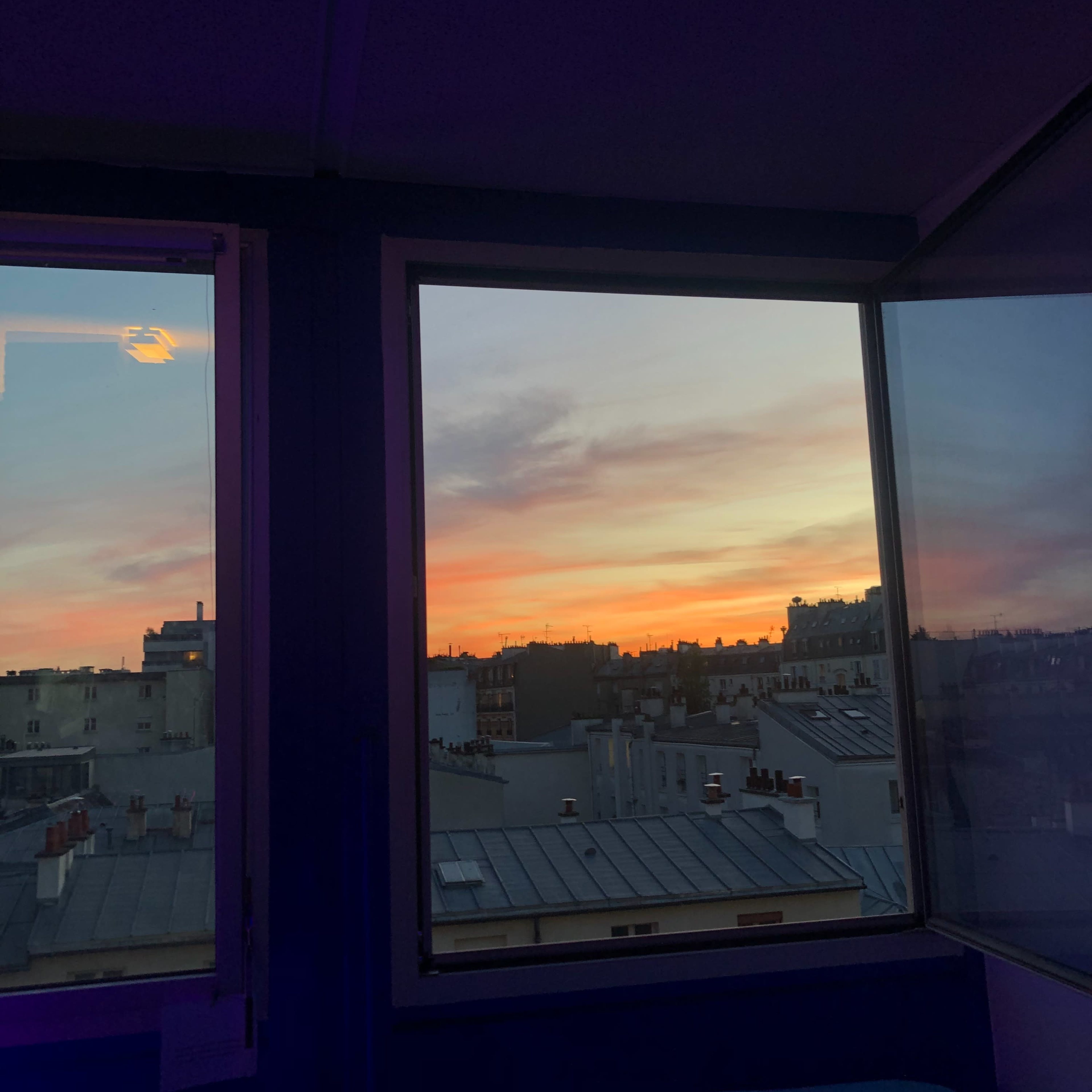 A panoramic view of a sunset over Paris rooftops framed by large windows.