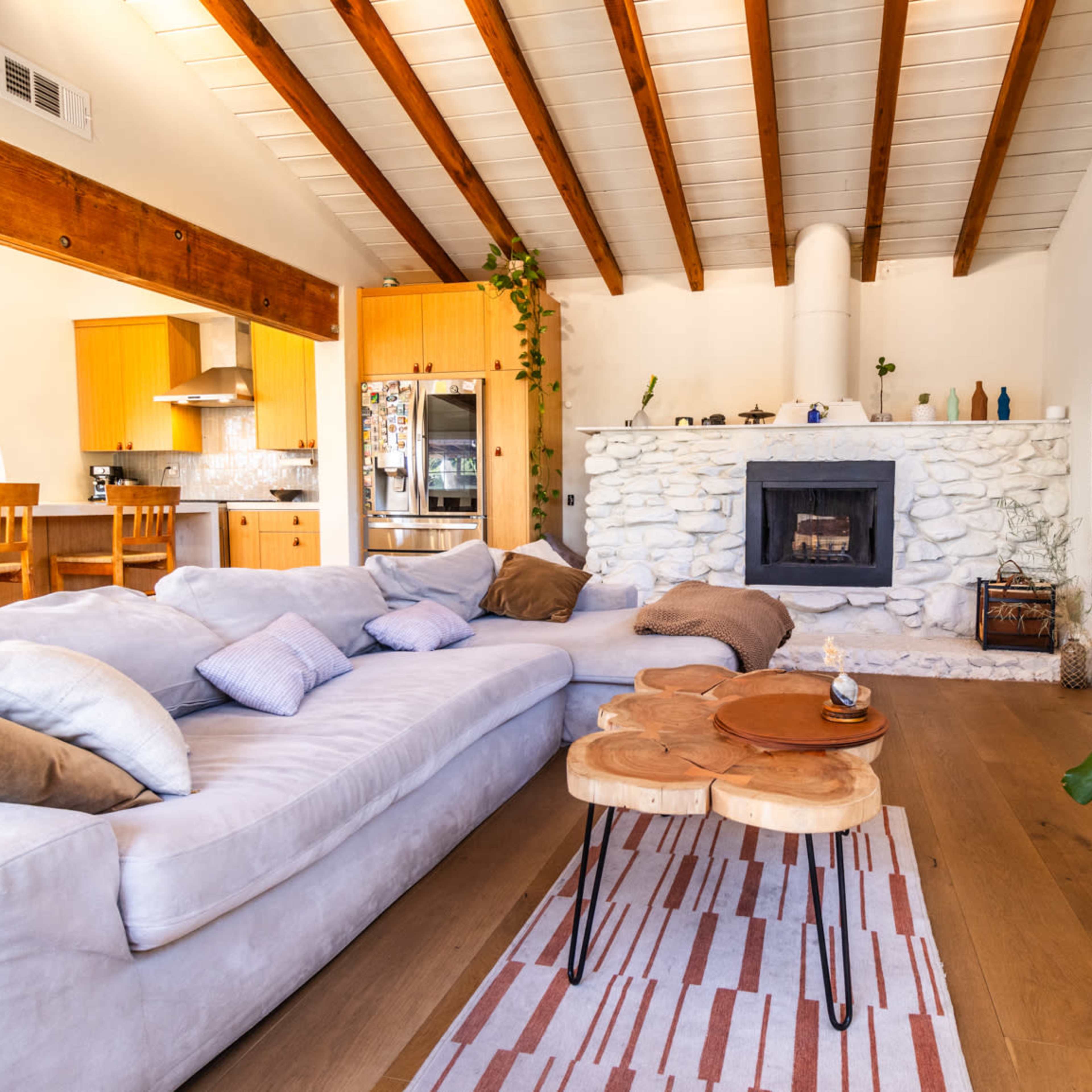 A cozy living room with a stone fireplace, a large sectional couch, and a wooden coffee table, featuring an open layout that connects to a kitchen area.