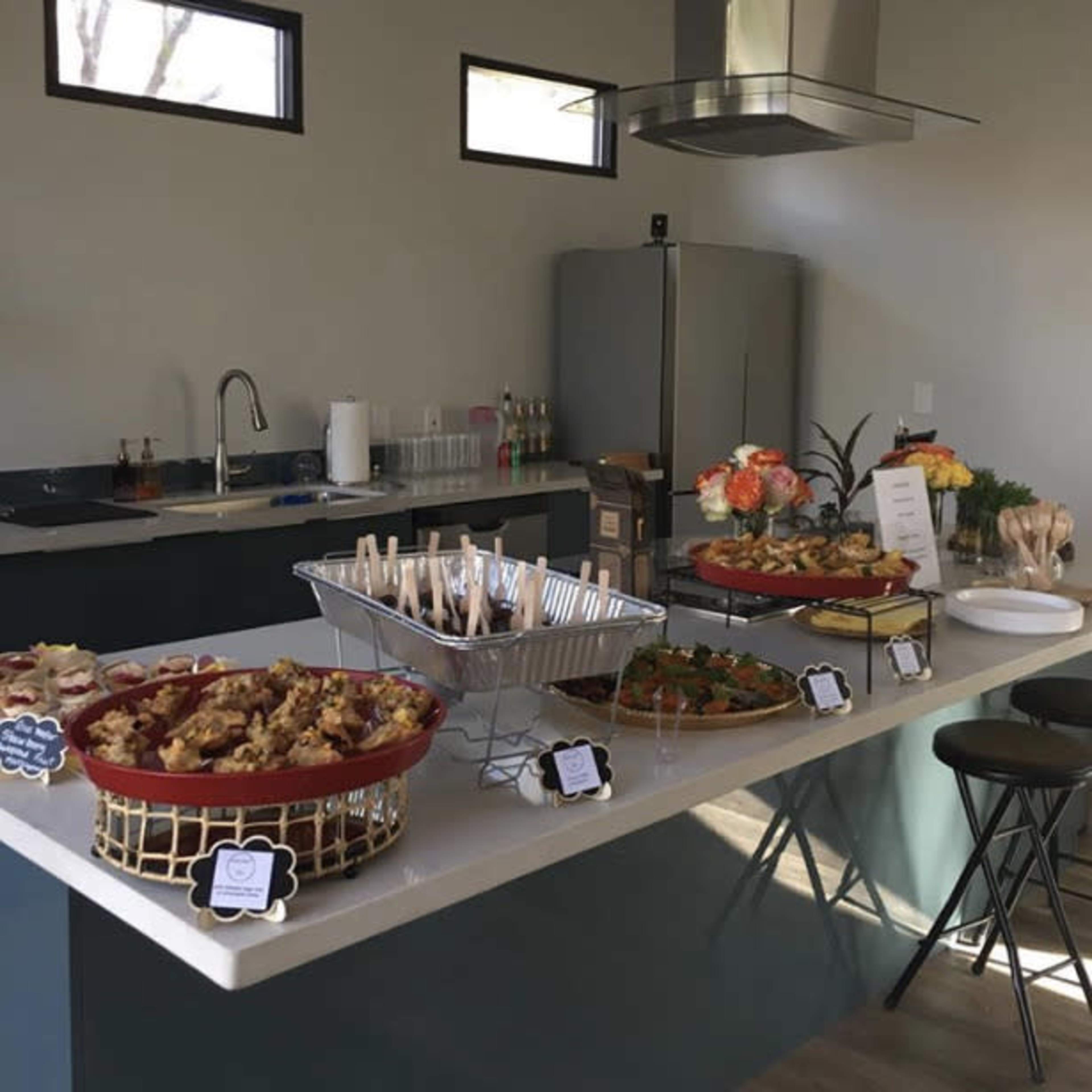 A modern kitchen is set up for a buffet, featuring a variety of dishes displayed on a counter alongside utensils and decorative items.