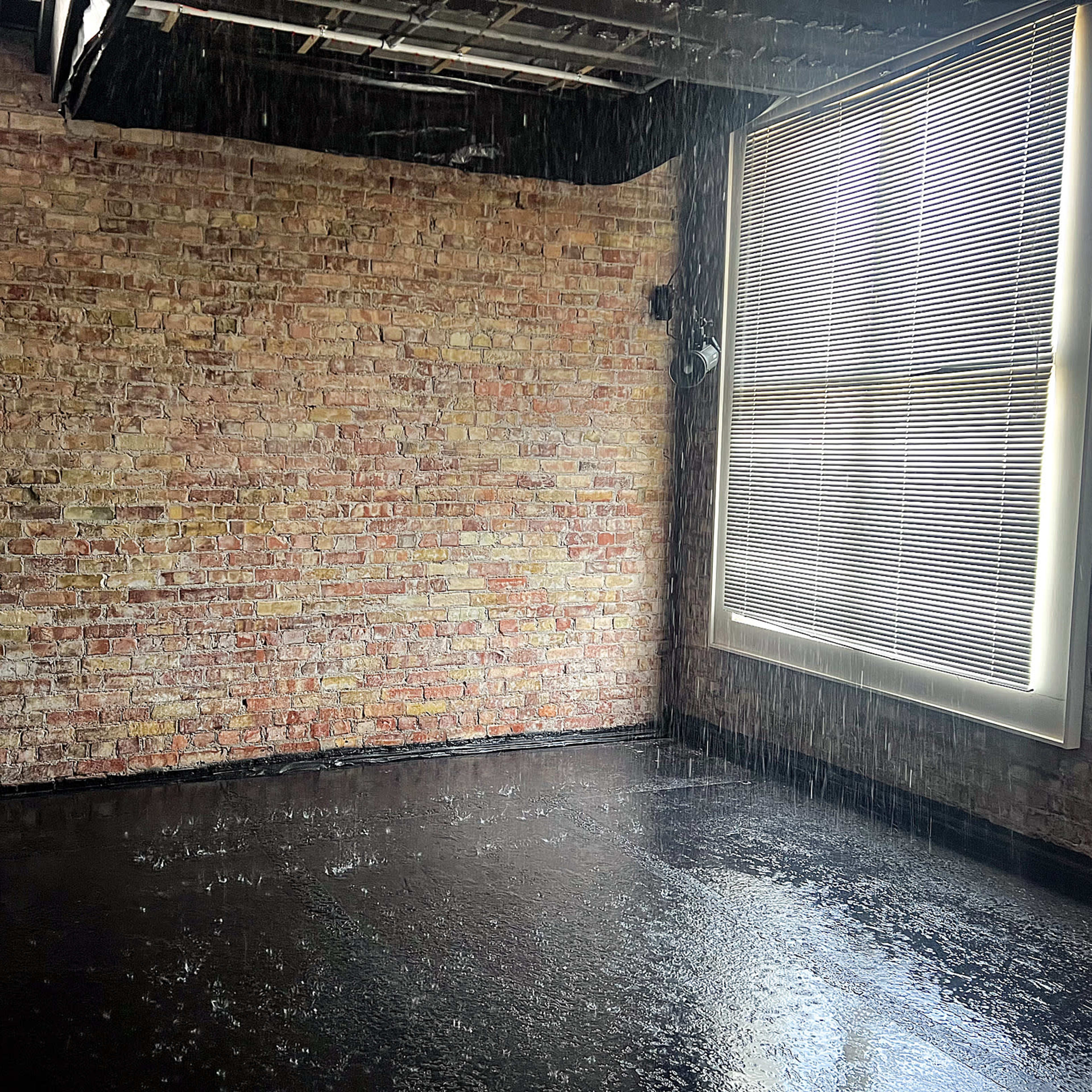 A room with exposed brick walls, a dark floor, and water cascading down from the ceiling.