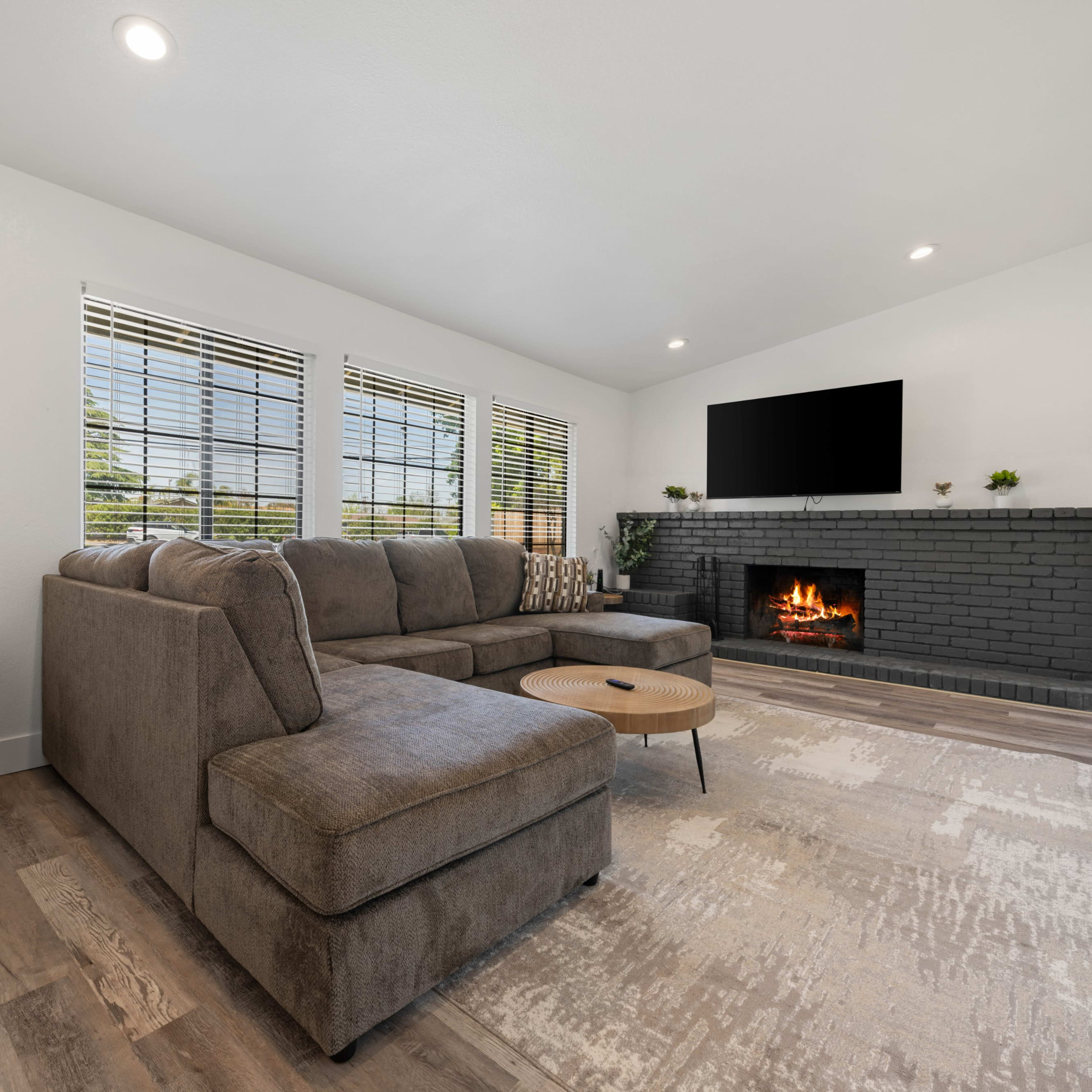 A cozy living room features a sectional sofa, a coffee table, a fireplace with a black brick surround, and a large mounted television on the wall.