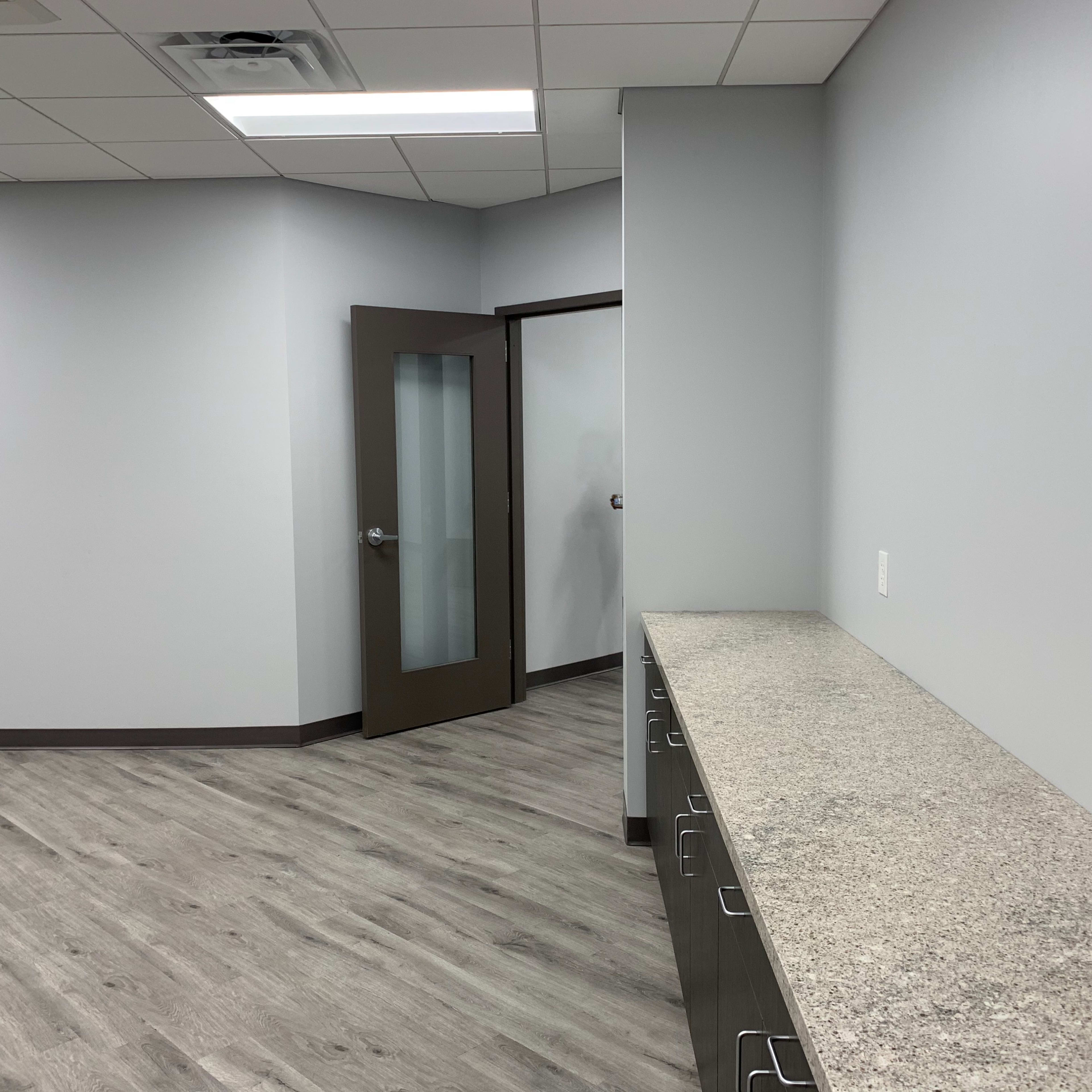 A modern, empty room with light gray walls, a long countertop along one wall, and a door leading to another room.