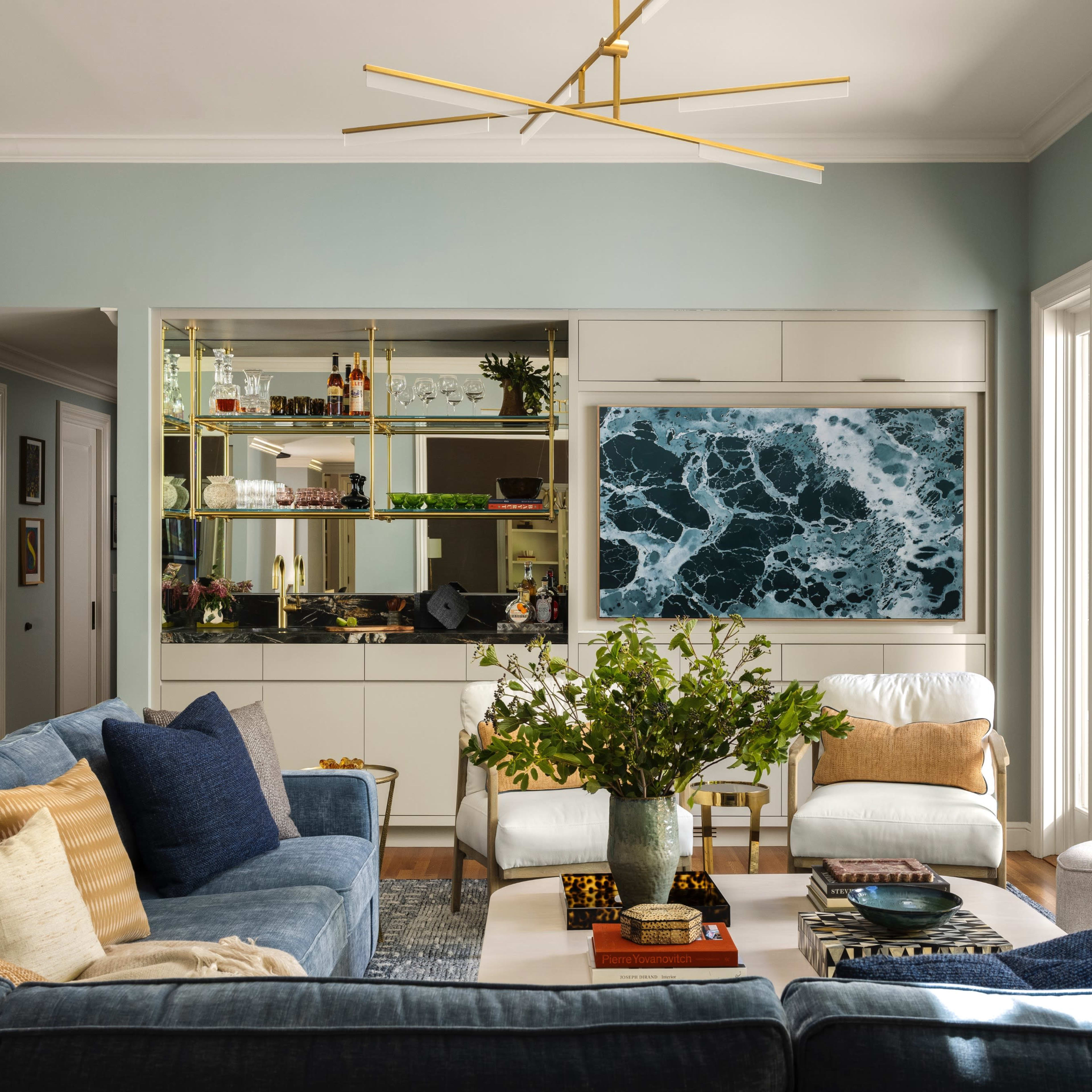 The living room features a blue sectional sofa, a coffee table with decorative items, and a wall unit displaying shelves and a large artwork depicting ocean waves.