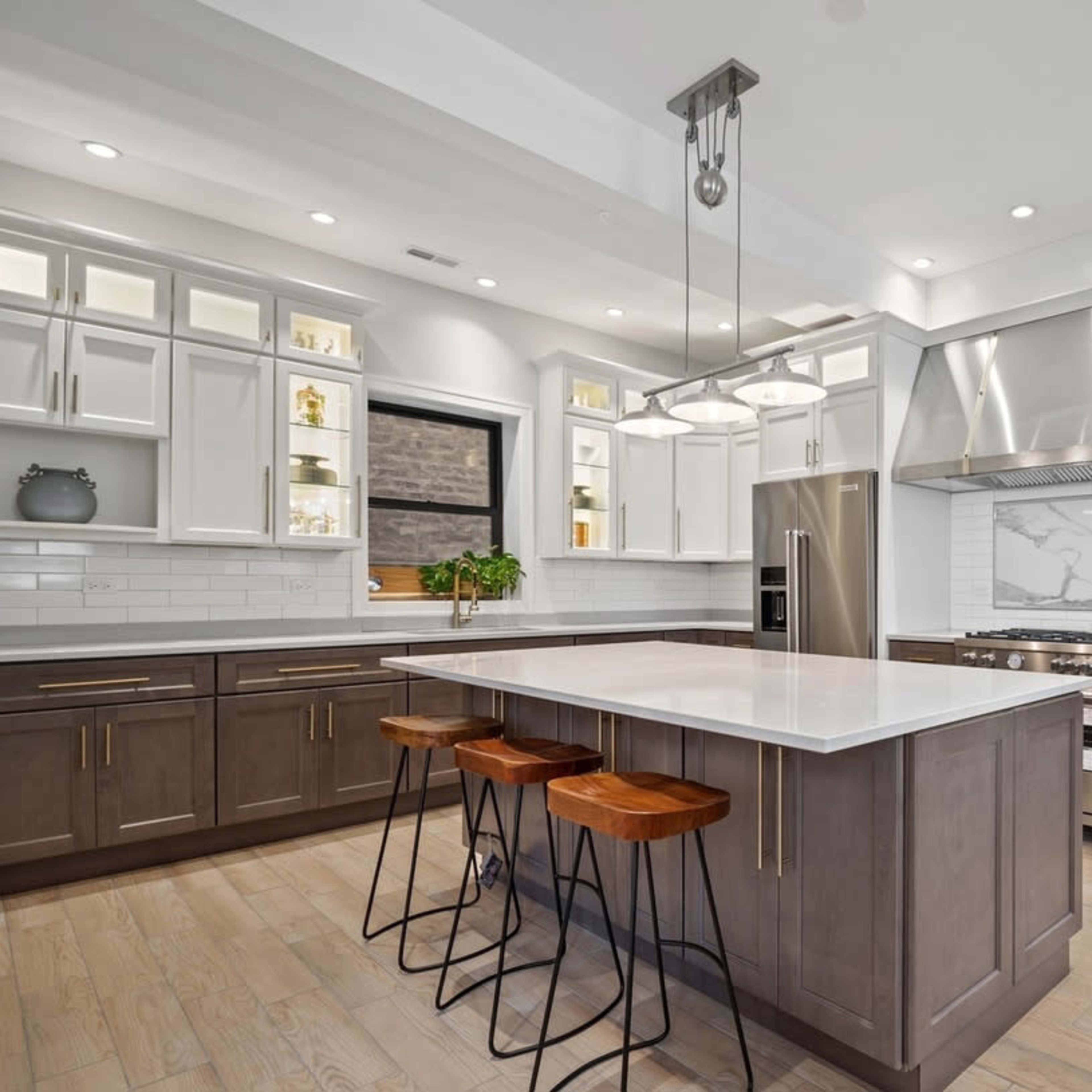 A modern kitchen featuring a large island with three bar stools, stainless steel appliances, and white cabinetry with a marble backsplash.