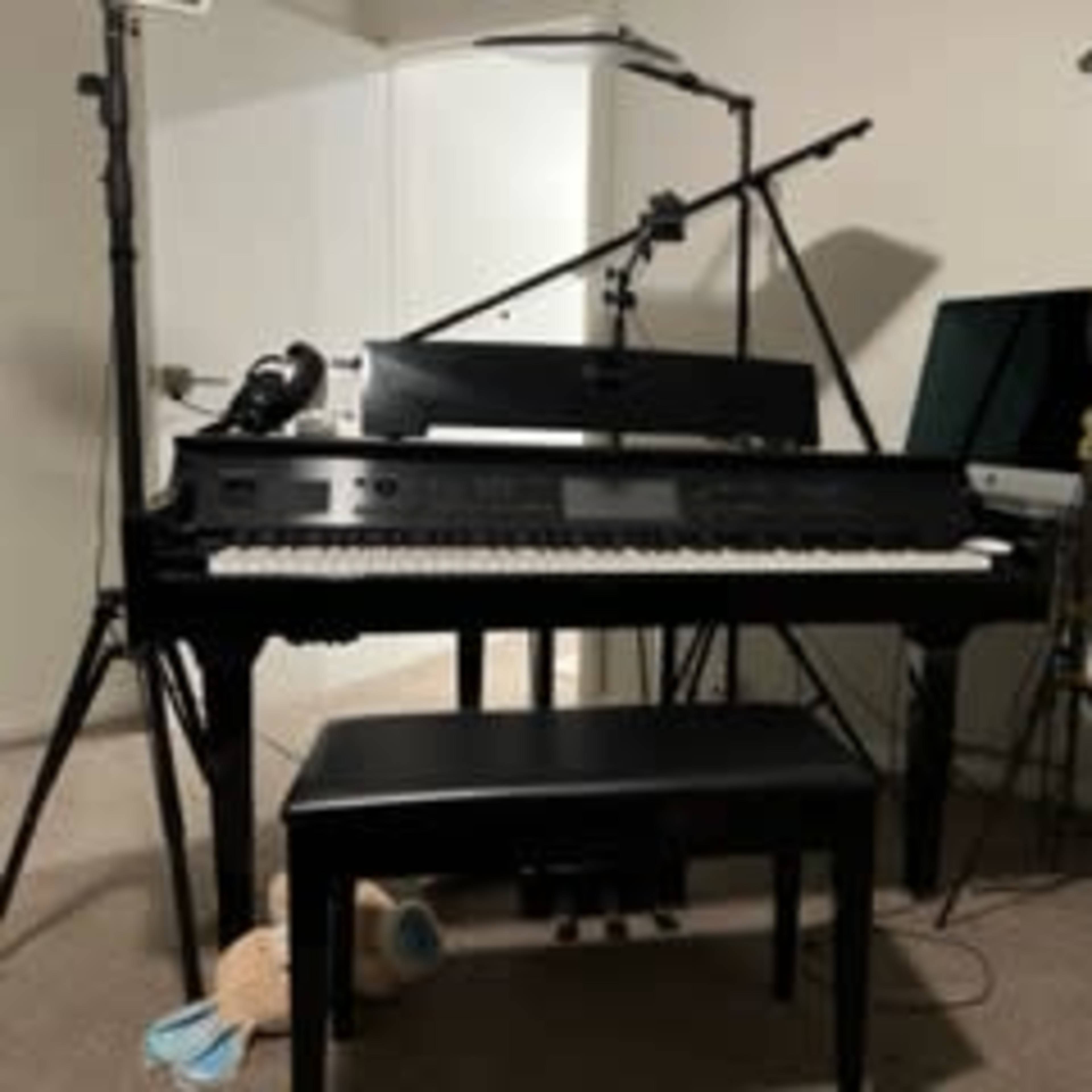 A black digital piano is positioned in a room, accompanied by a bench, music stand, and studio lighting equipment.