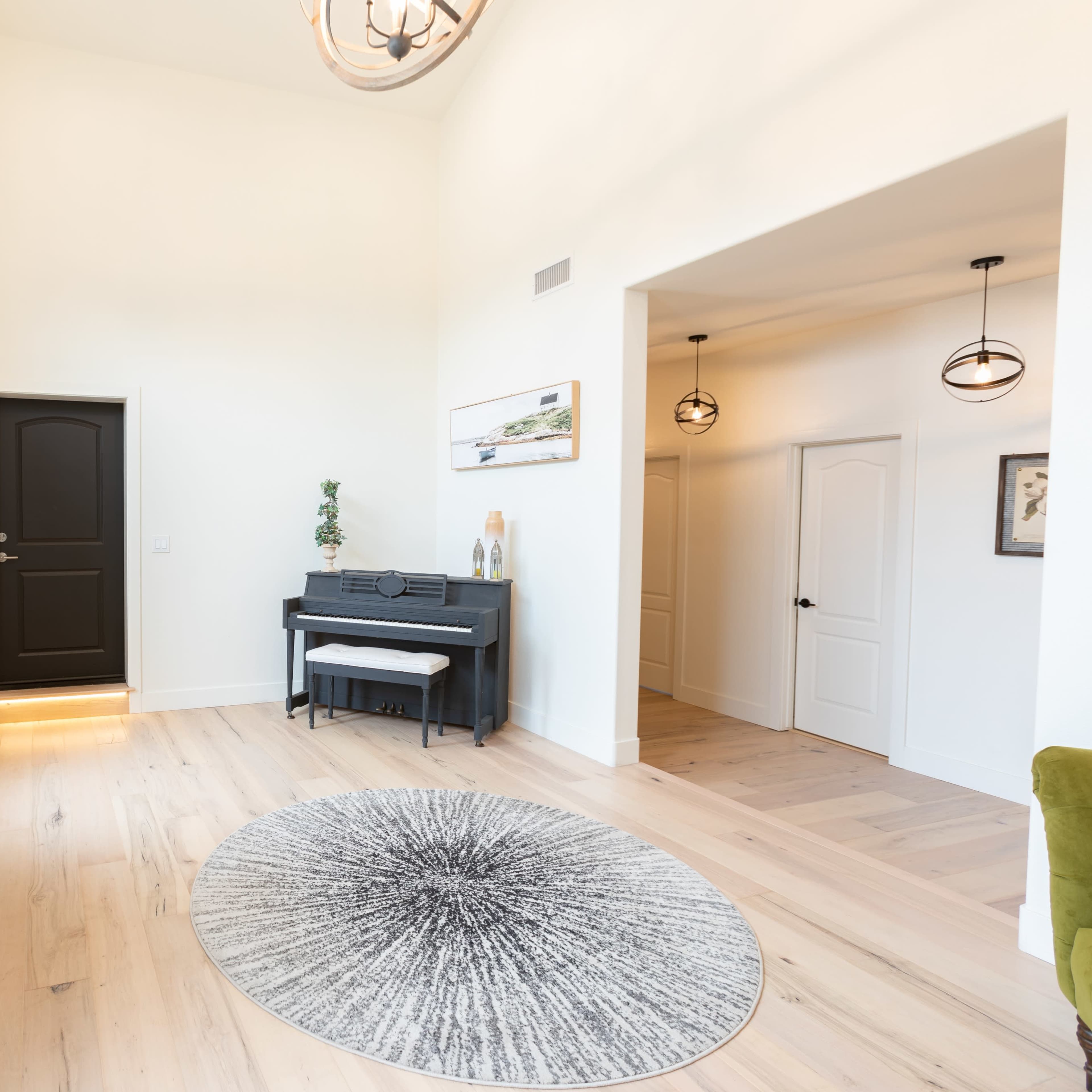 A bright entryway with a black piano, a round rug, and doors leading to other rooms.