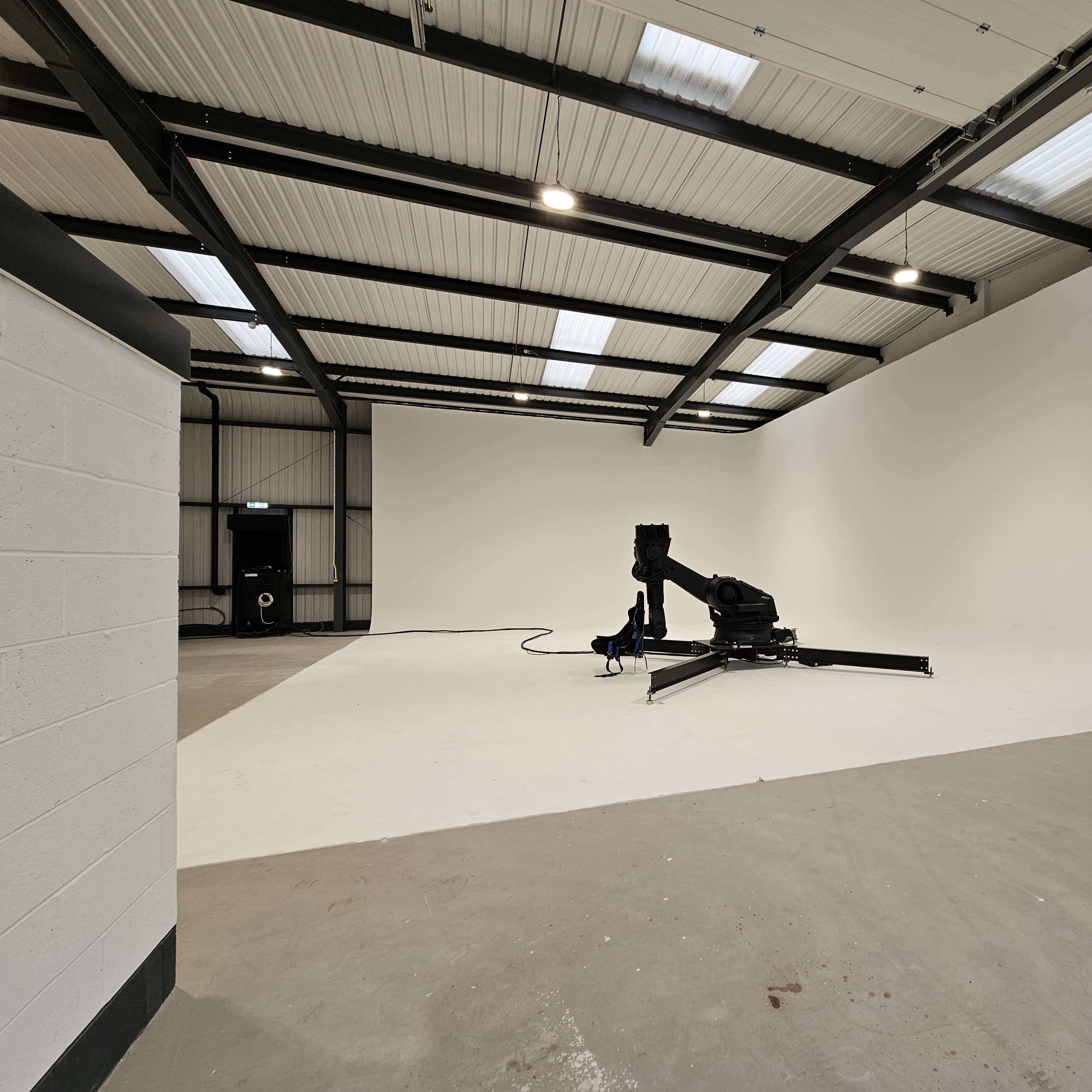 A spacious studio features a large white backdrop and a stand for equipment in the center.