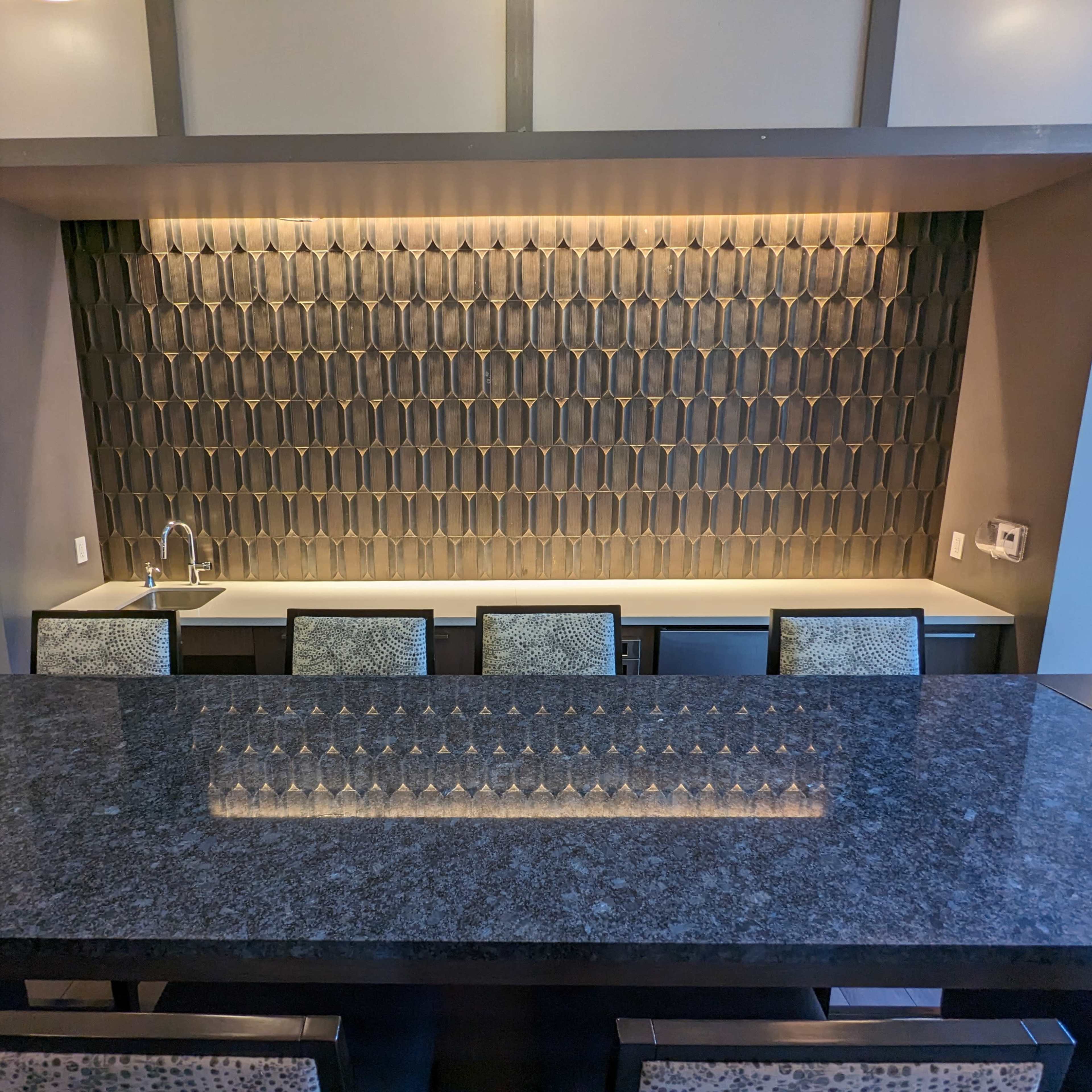 A modern kitchen featuring a countertop bar with four chairs and a tiled backsplash illuminated by soft lighting.