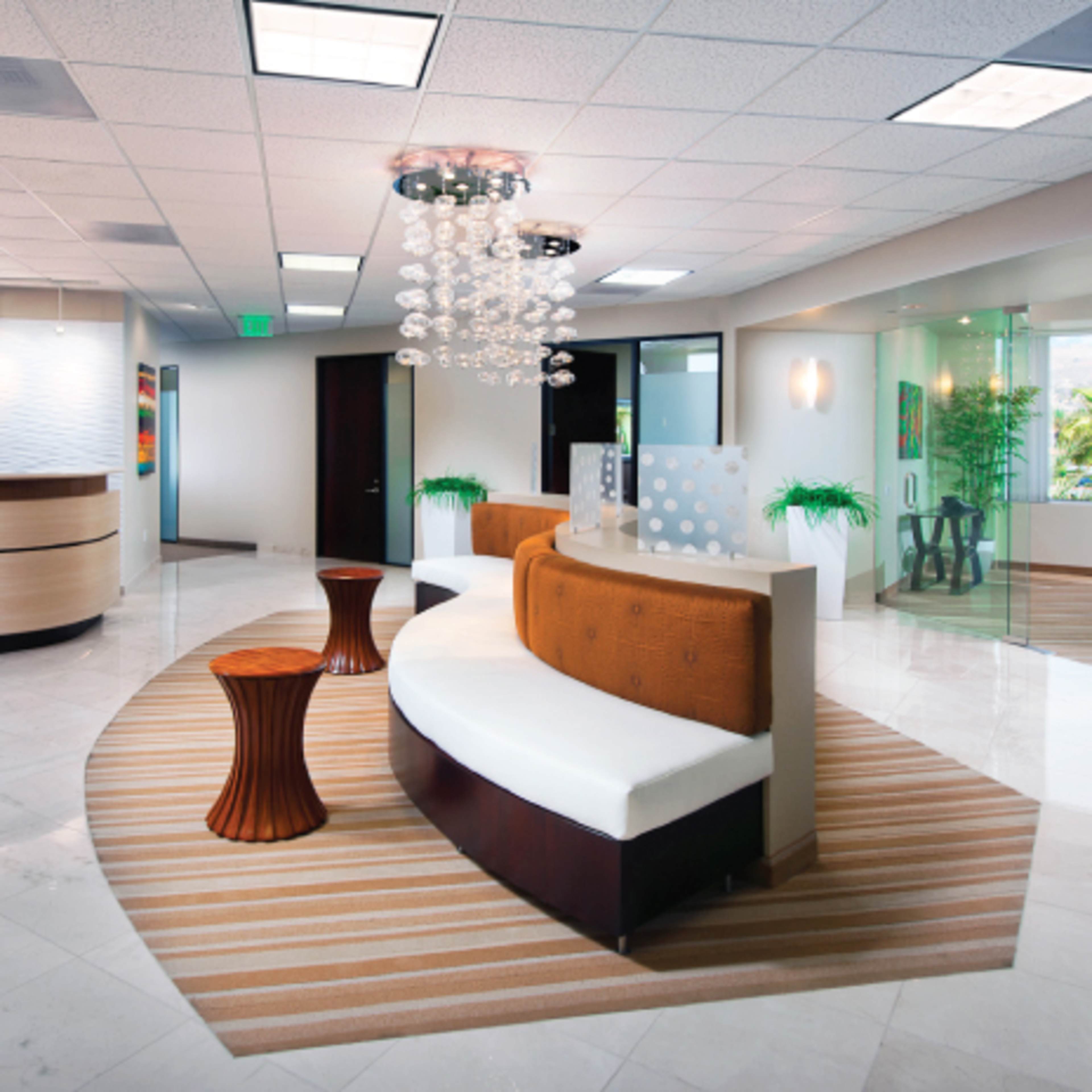 A modern reception area with a curved seating arrangement, a circular ceiling light fixture, and large windows offering a view of greenery outside.