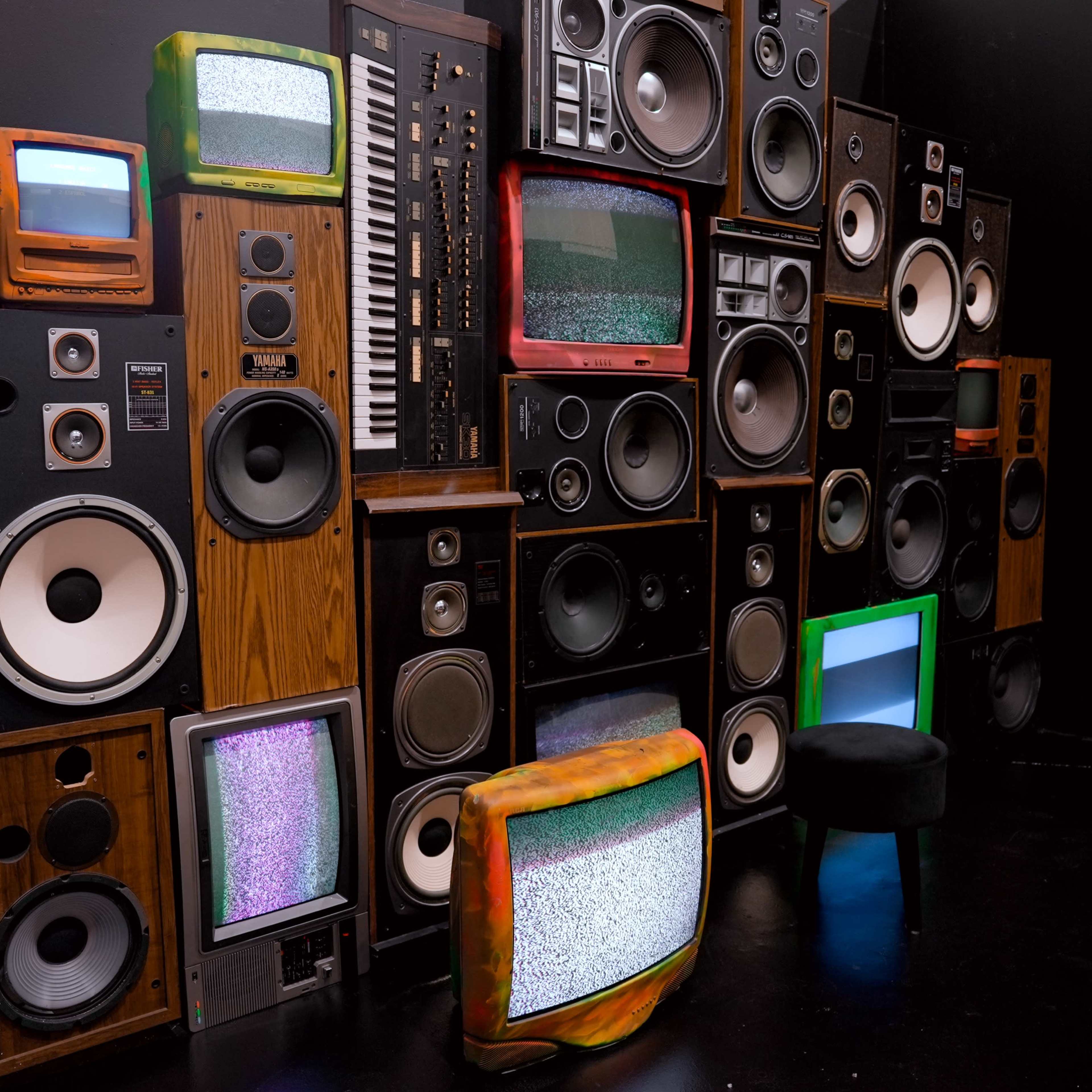 A wall of vintage televisions and speakers arranged in a collage against a black background.